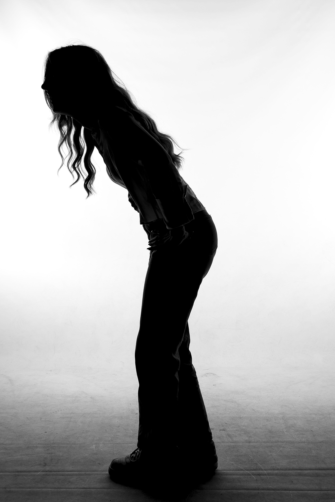 Silhouette of a woman bending forward with long, wavy hair against a plain white background.