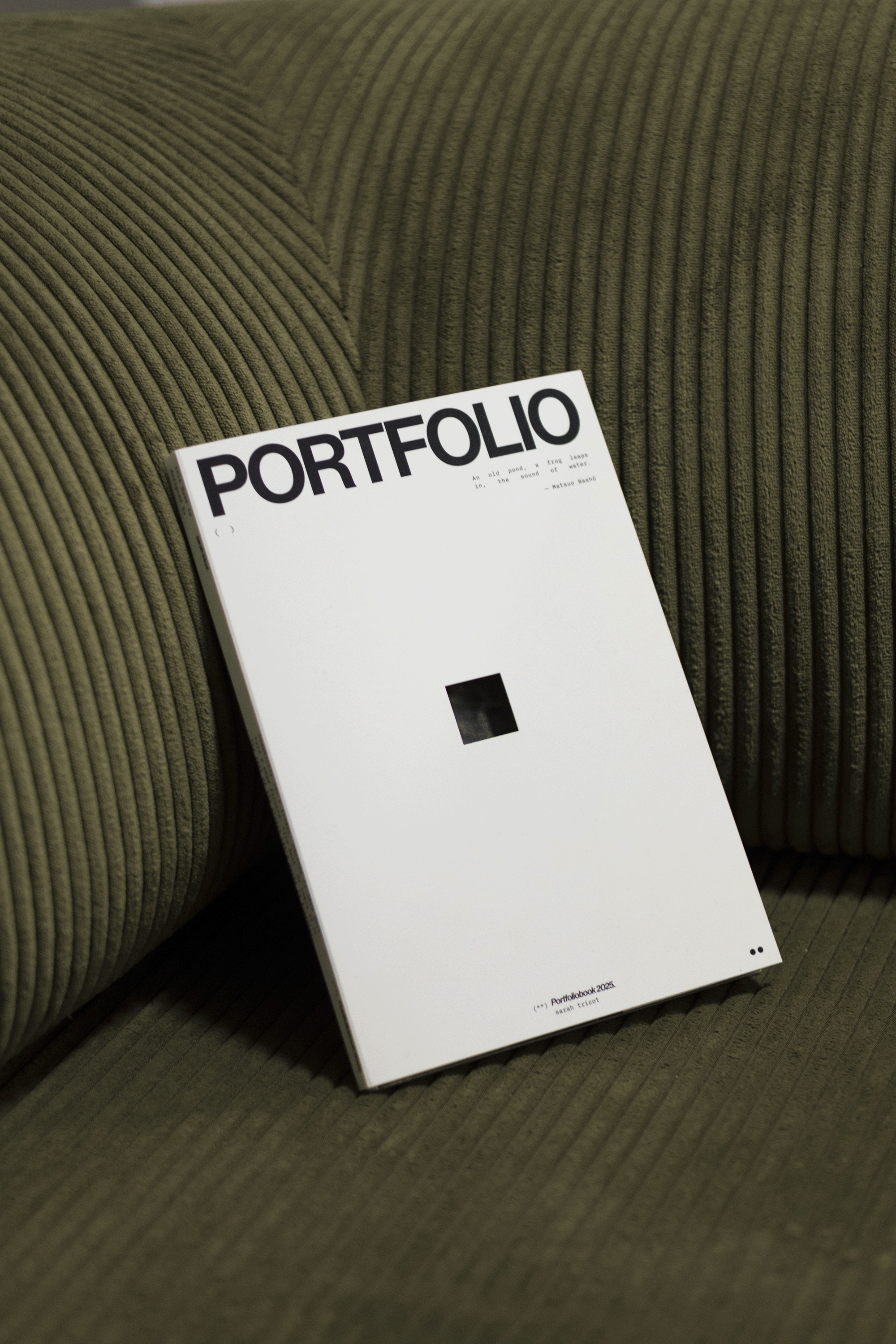 A white portfolio book with black text titled 'PORTFOLIO' resting on a textured green fabric surface.
