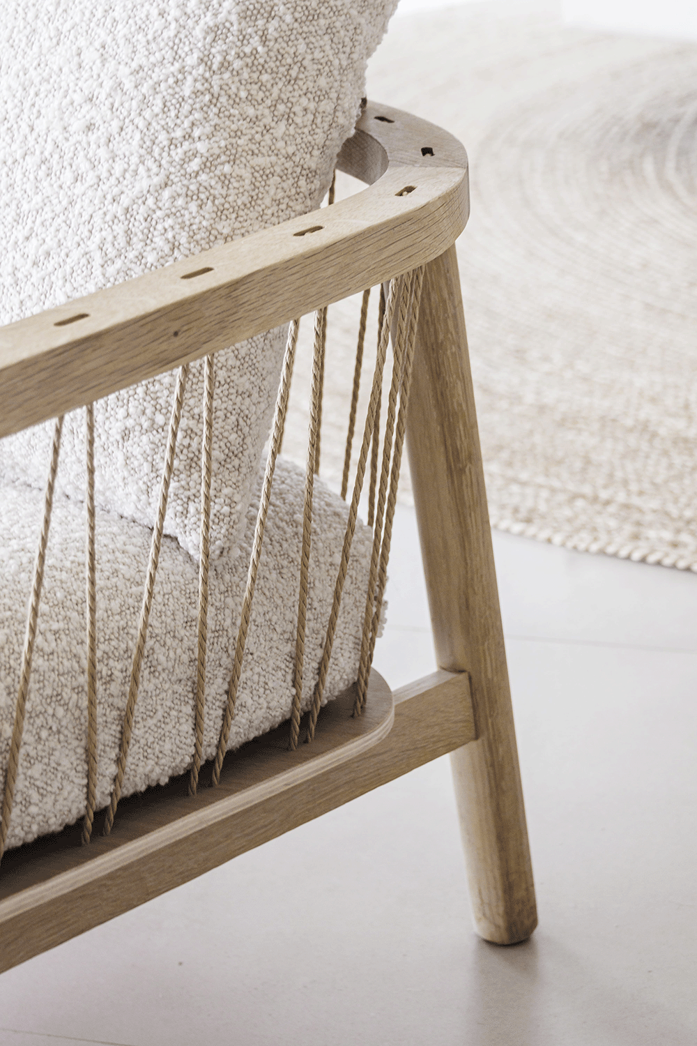 Close-up of a wooden and rope chair with a textured white cushion, part of a beige circular rug in the background.