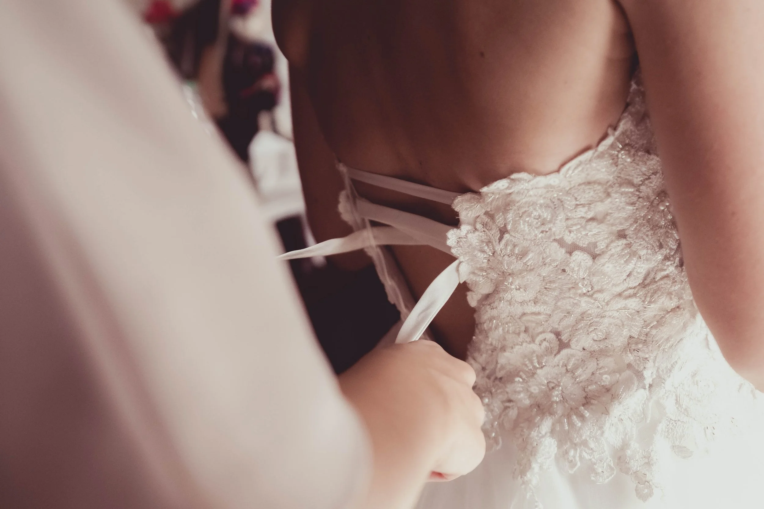 Close-up of a bride's back, showing her wedding dress with lace and ribbon details.