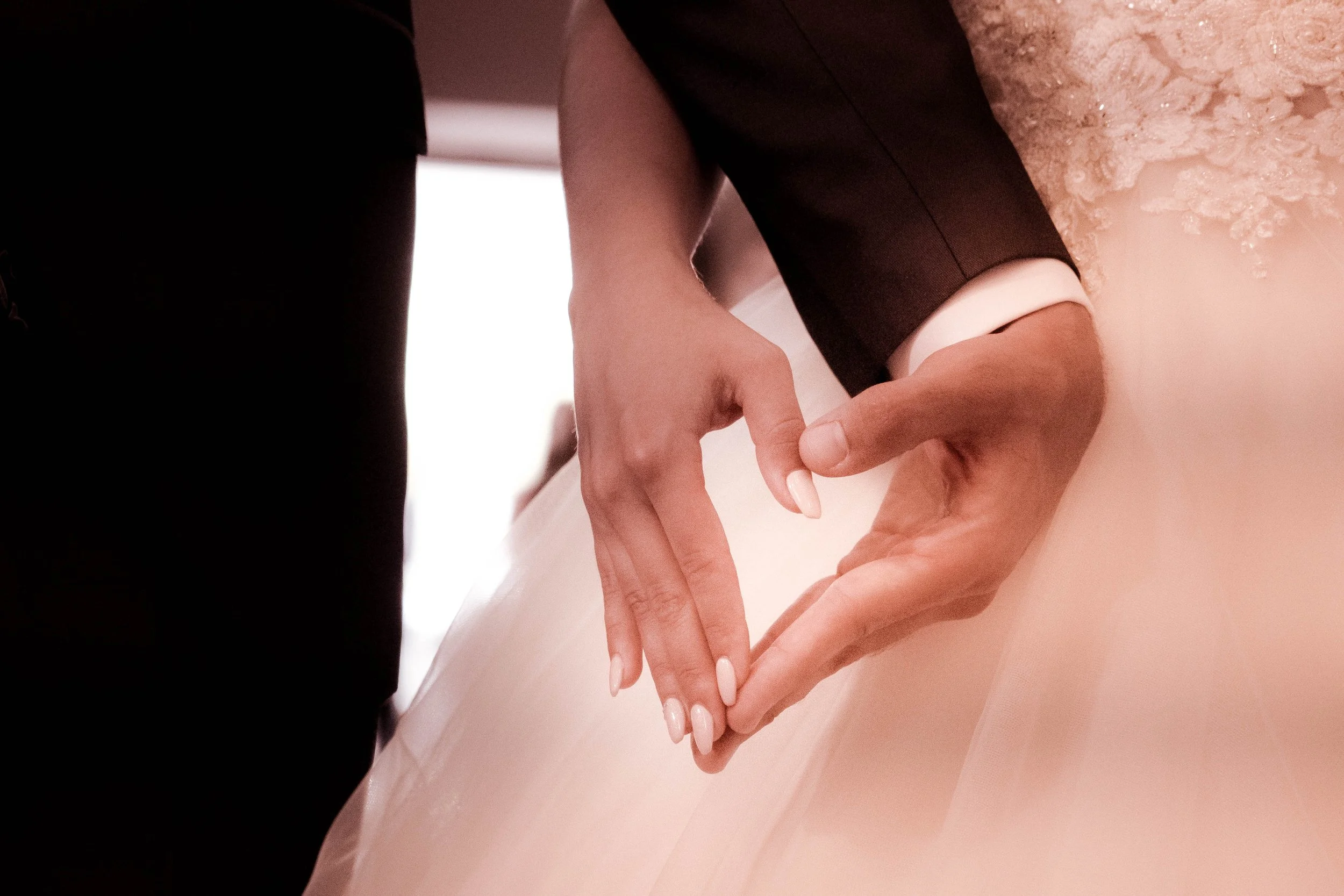 A close-up of a couple holding hands, with the woman wearing a wedding dress, during a wedding ceremony.