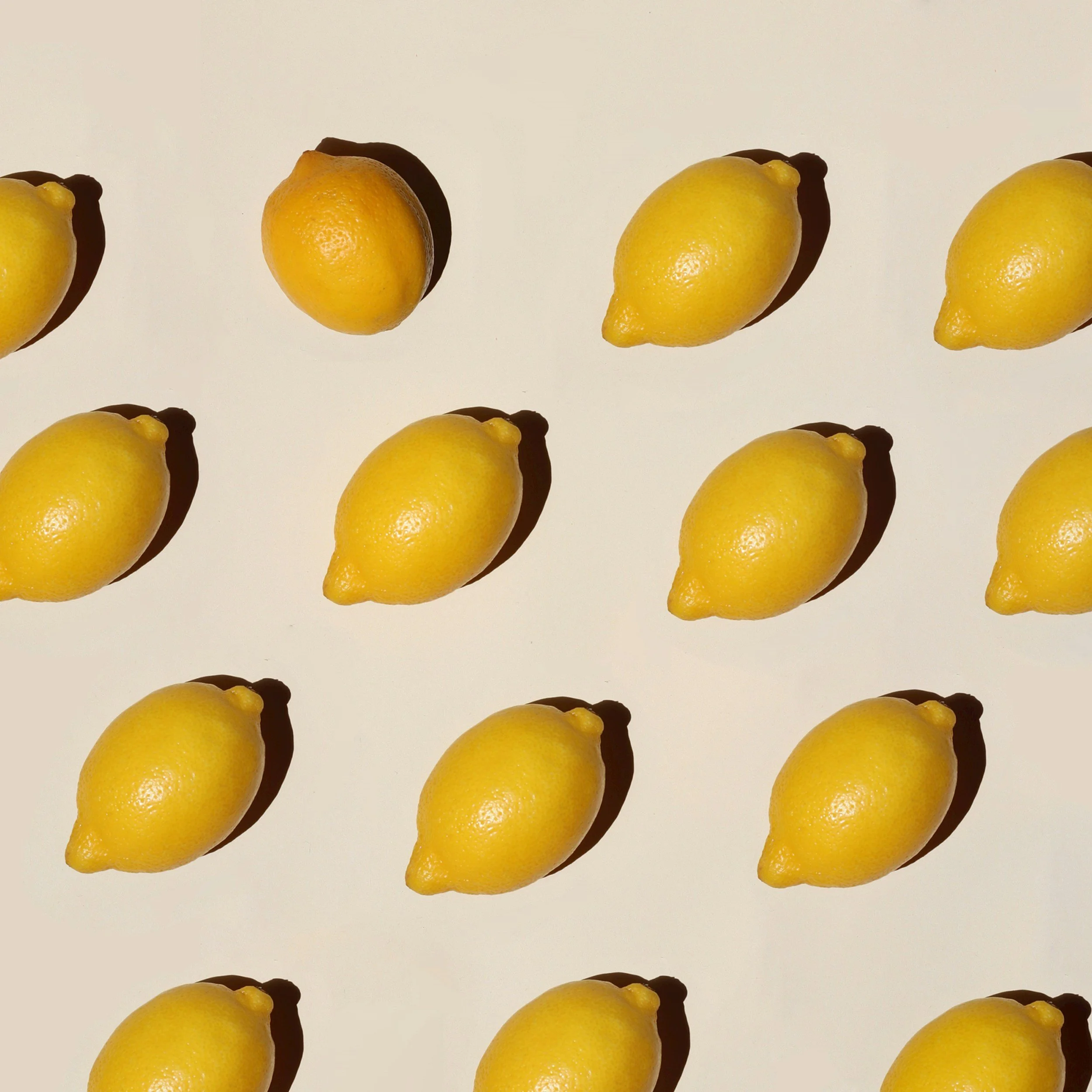 Multiple lemons arranged in a pattern on a light background, with shadows cast beside each lemon.