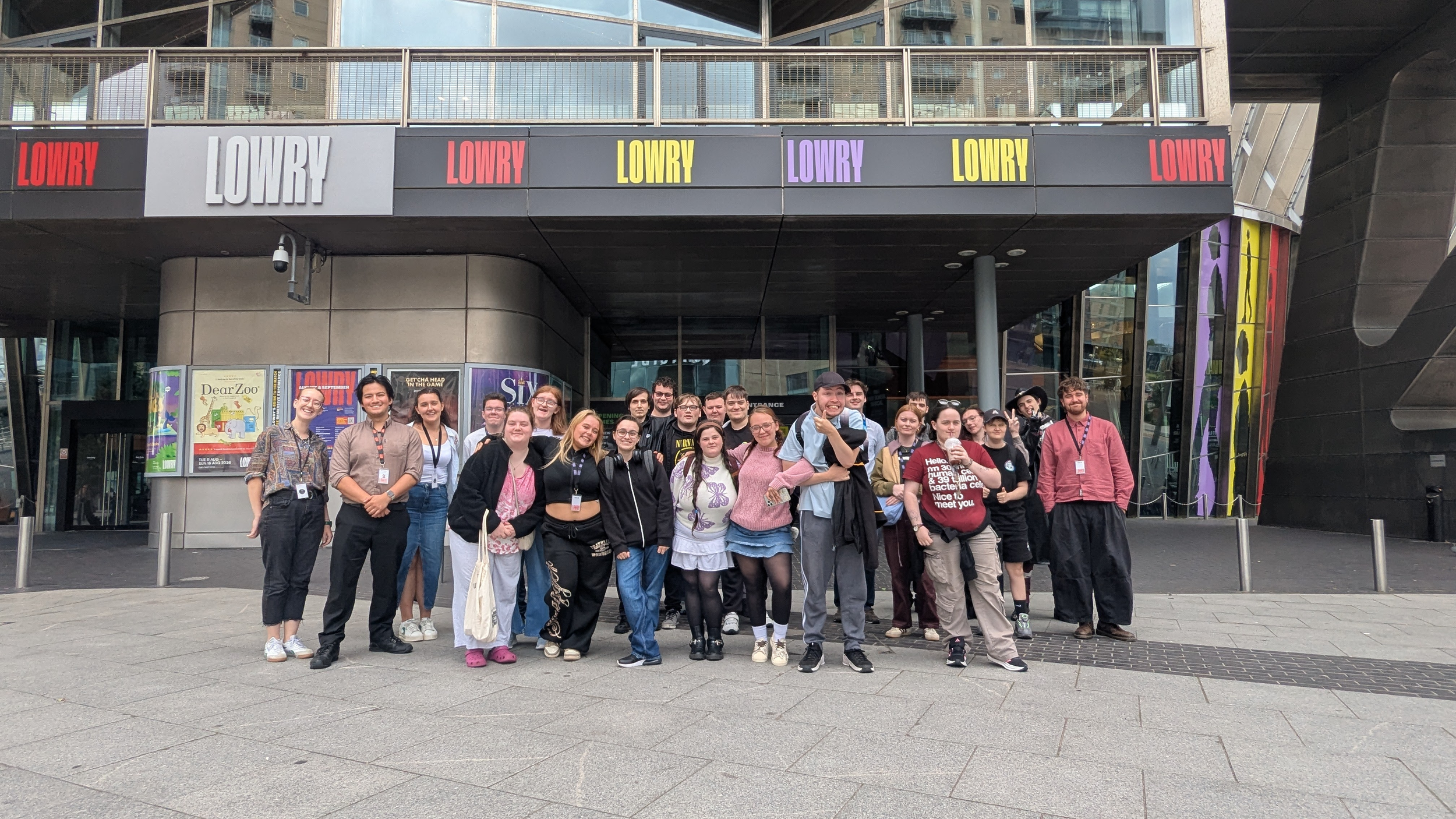 Group of people standing together outside a modern building with large glass windows and balconies. Some people are smiling and wearing casual clothing.