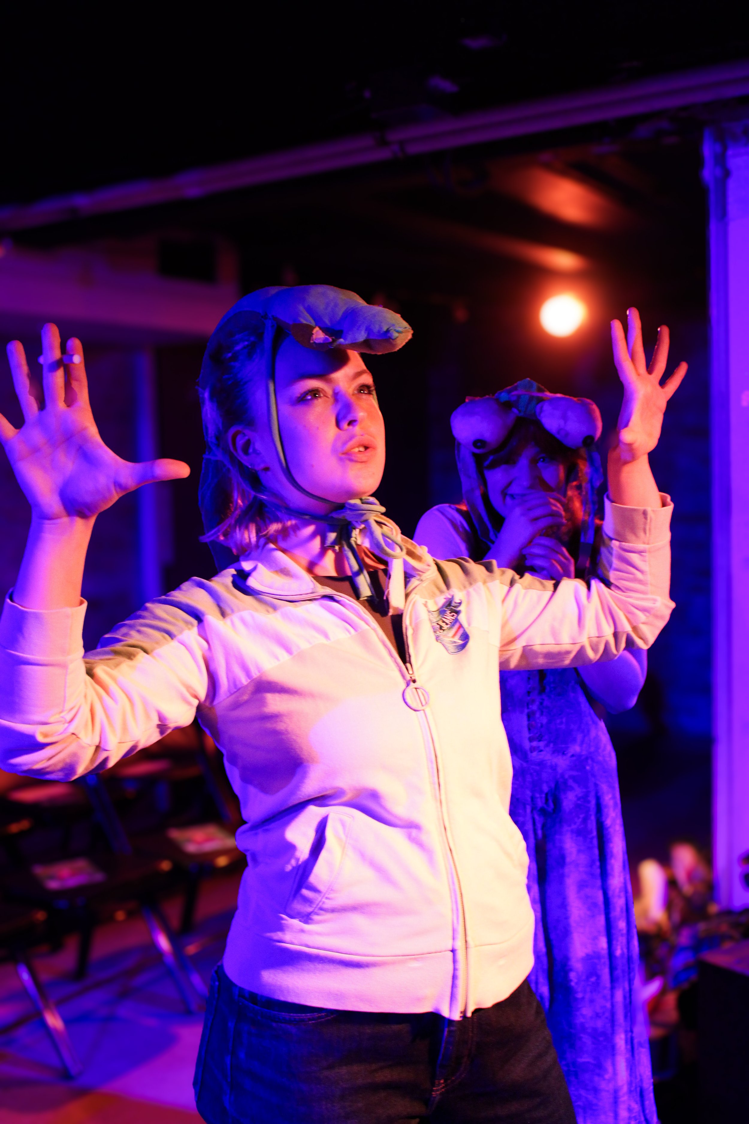 Two people with frog hats dancing under colorful purple and red lights, in a dark indoor setting.
