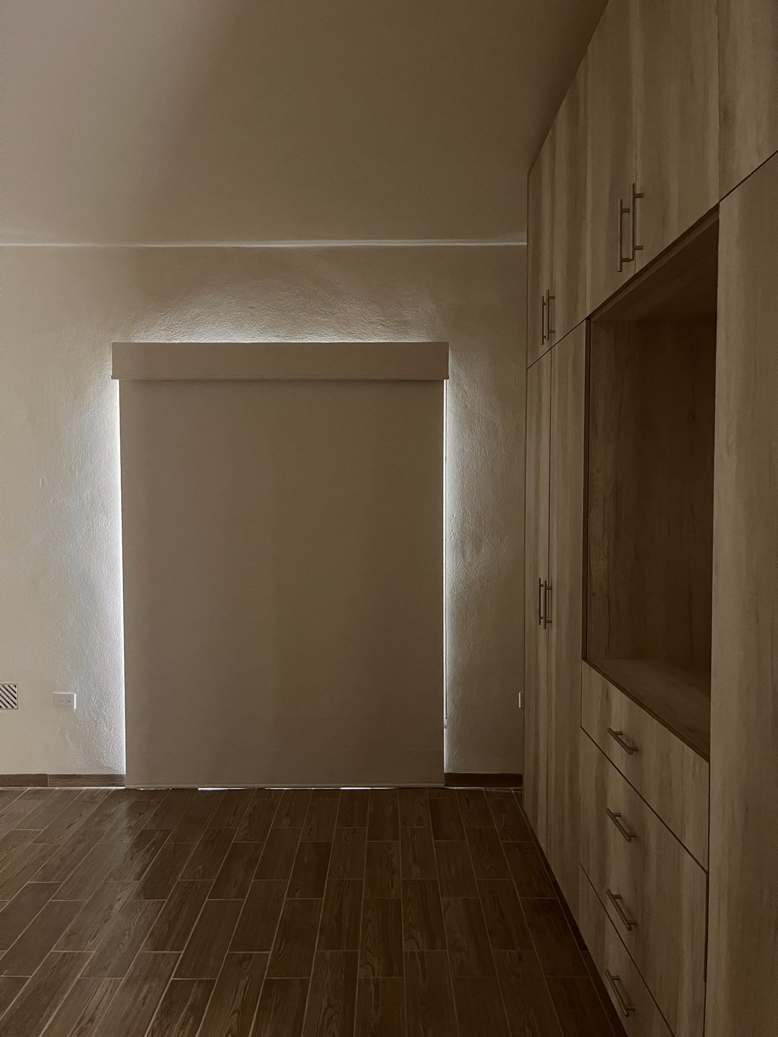 Imagen de una habitación vacía con armario de madera y suelo de baldosas de color marrón. Al fondo, una persiana enrollable blackout cubre una ventana para dar privacidad, y oscuridad. Casa ubicada en fraccionamiento de San Miguel de Allende.