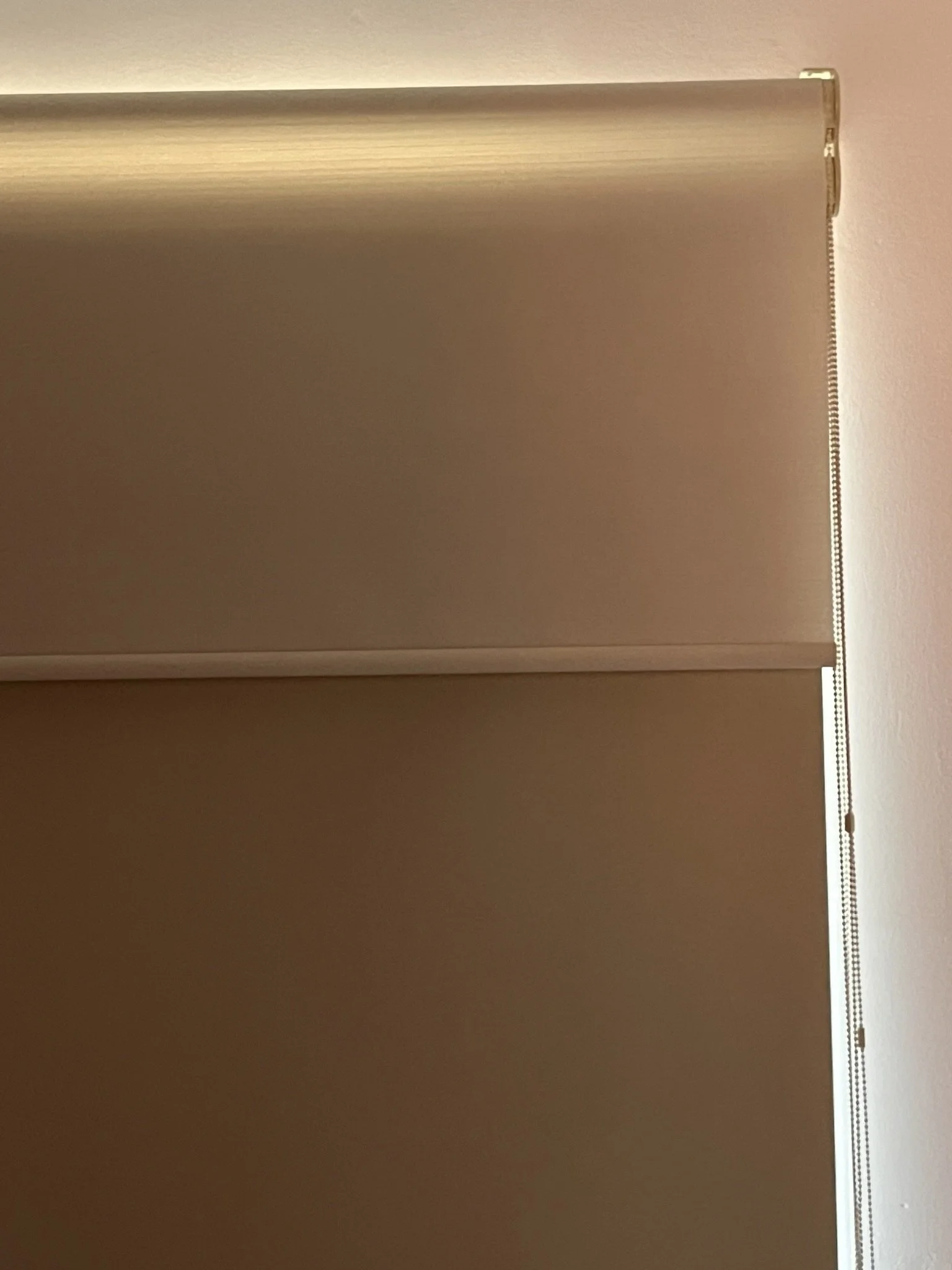 Persiana vertical de color beige en una ventana, con pared de color rosa claro.
