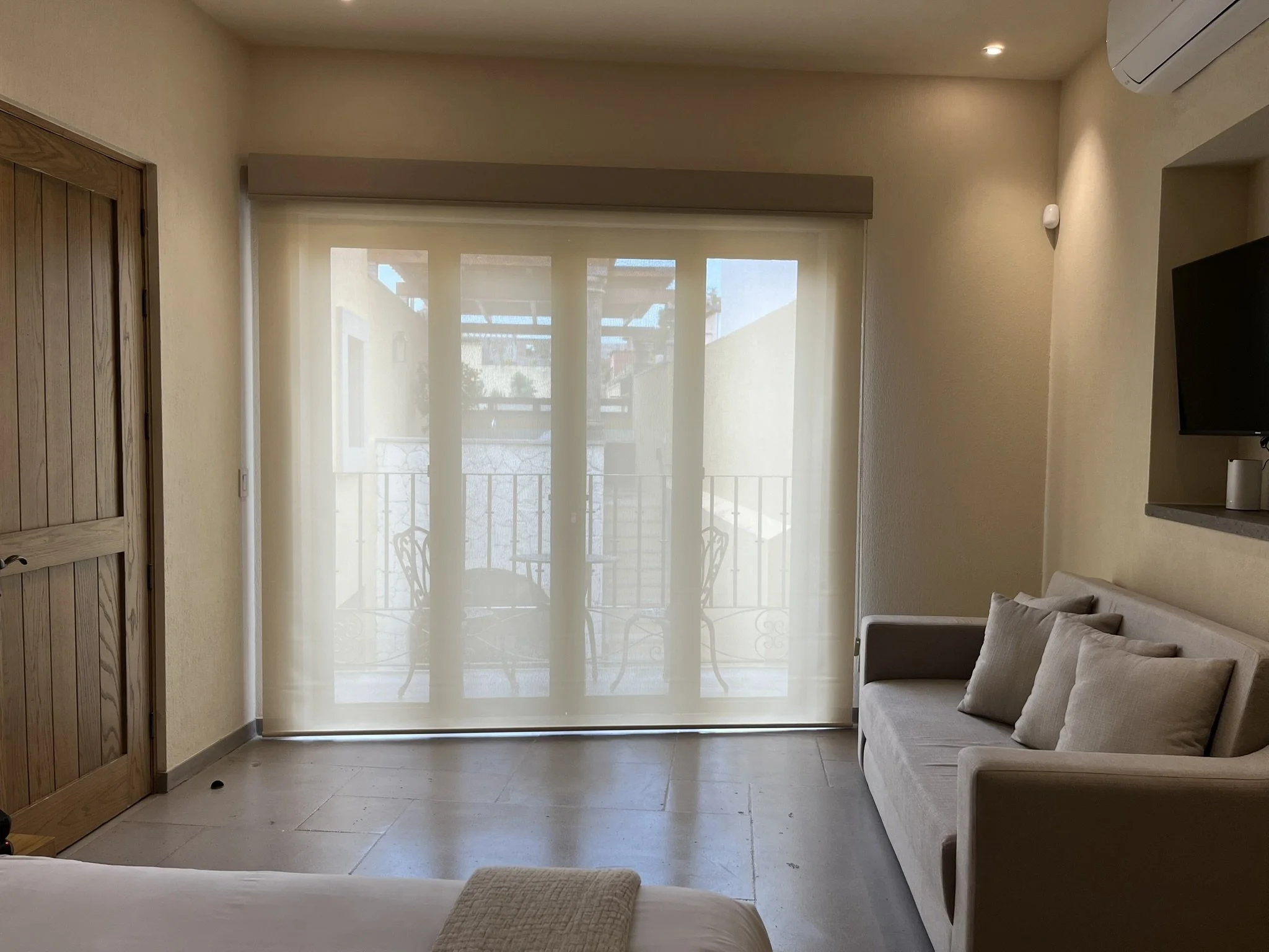 Sala de estar con sofá de color crema, ventana con cortinas translúcidas, puertas de madera y aire acondicionado en la esquina. Fraccionamiento en San Miguel de Allende.
