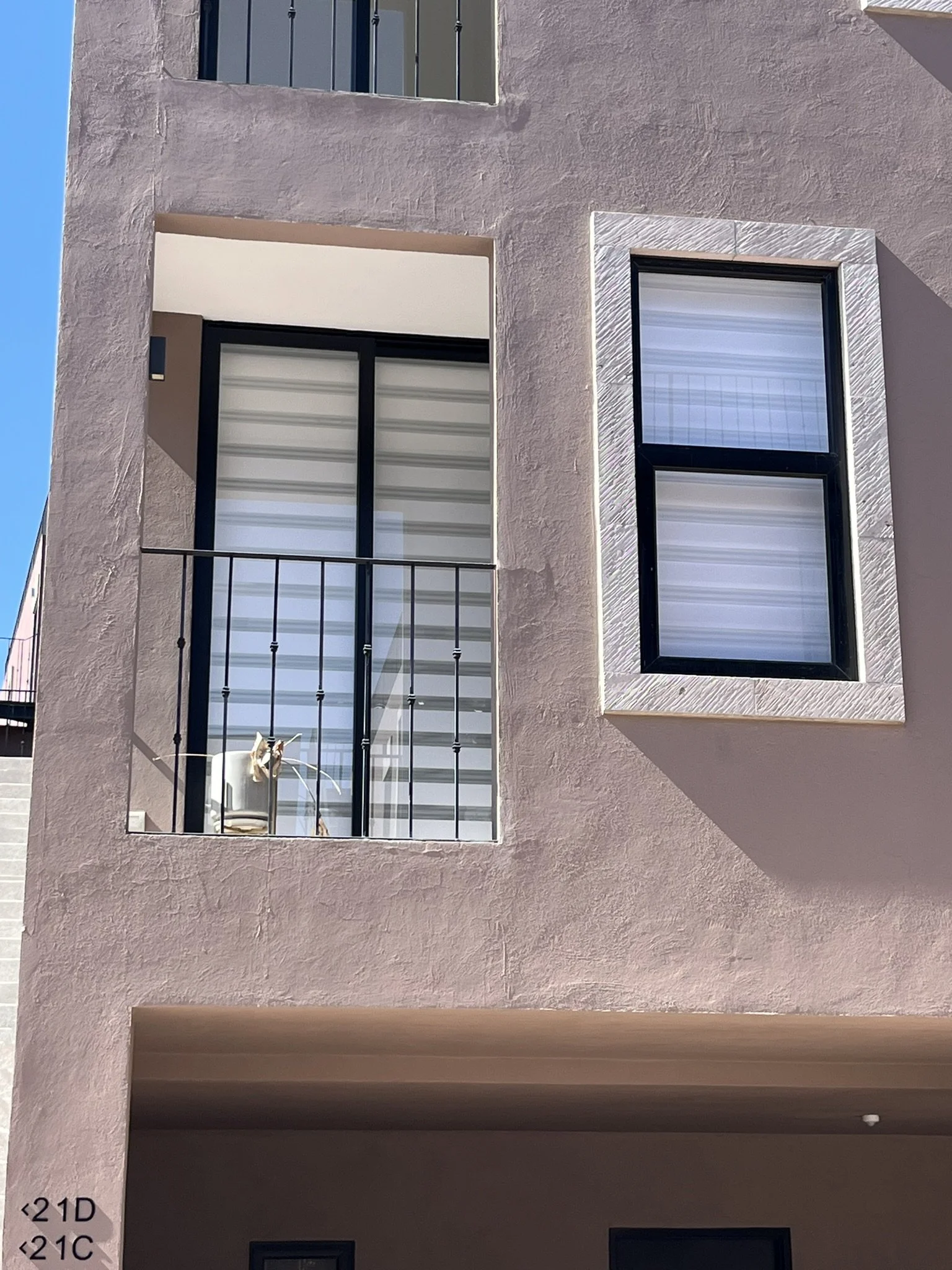 Fachada de un edificio moderno con ventanas y balcones, paredes de color rosa claro y marcos de ventana oscuros. En la ventana se muestra una persiana estilo Sheer Elegance. Apartamento en San Miguel de Allende.