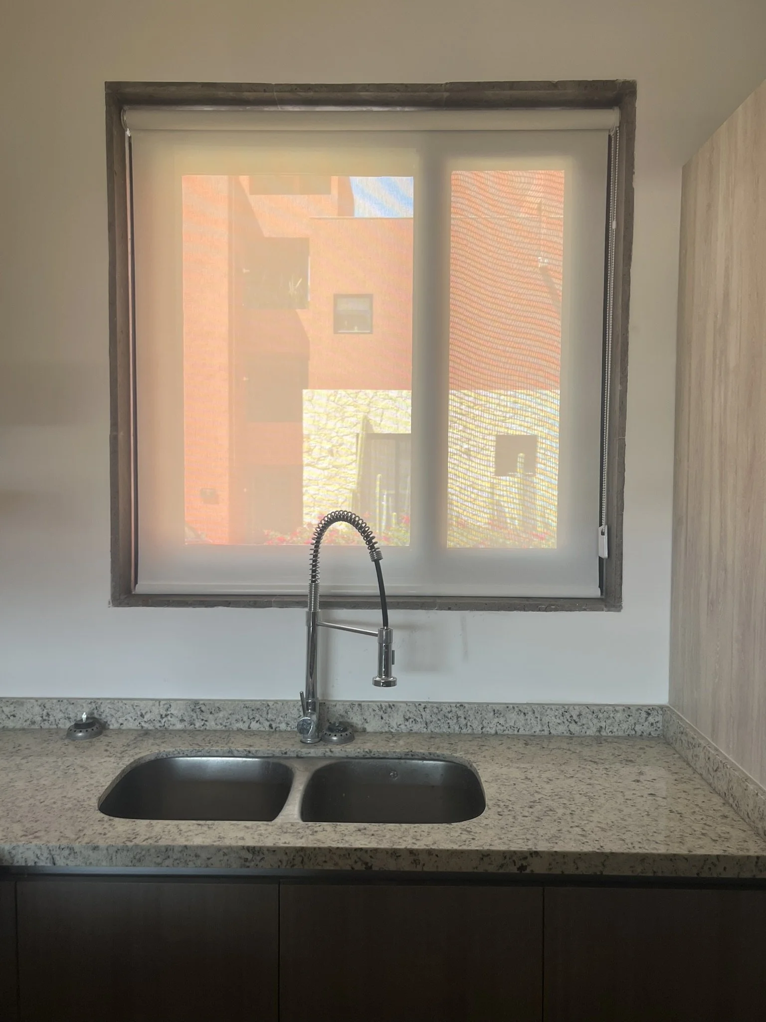 Vista de una cocina con fregadero, grifo y ventana con persiana enrollable de malla solar de protección en la parte superior del fregadero. Se observa una encimera de granito y mueble debajo. Fraccionamiento en San Miguel de Allende.