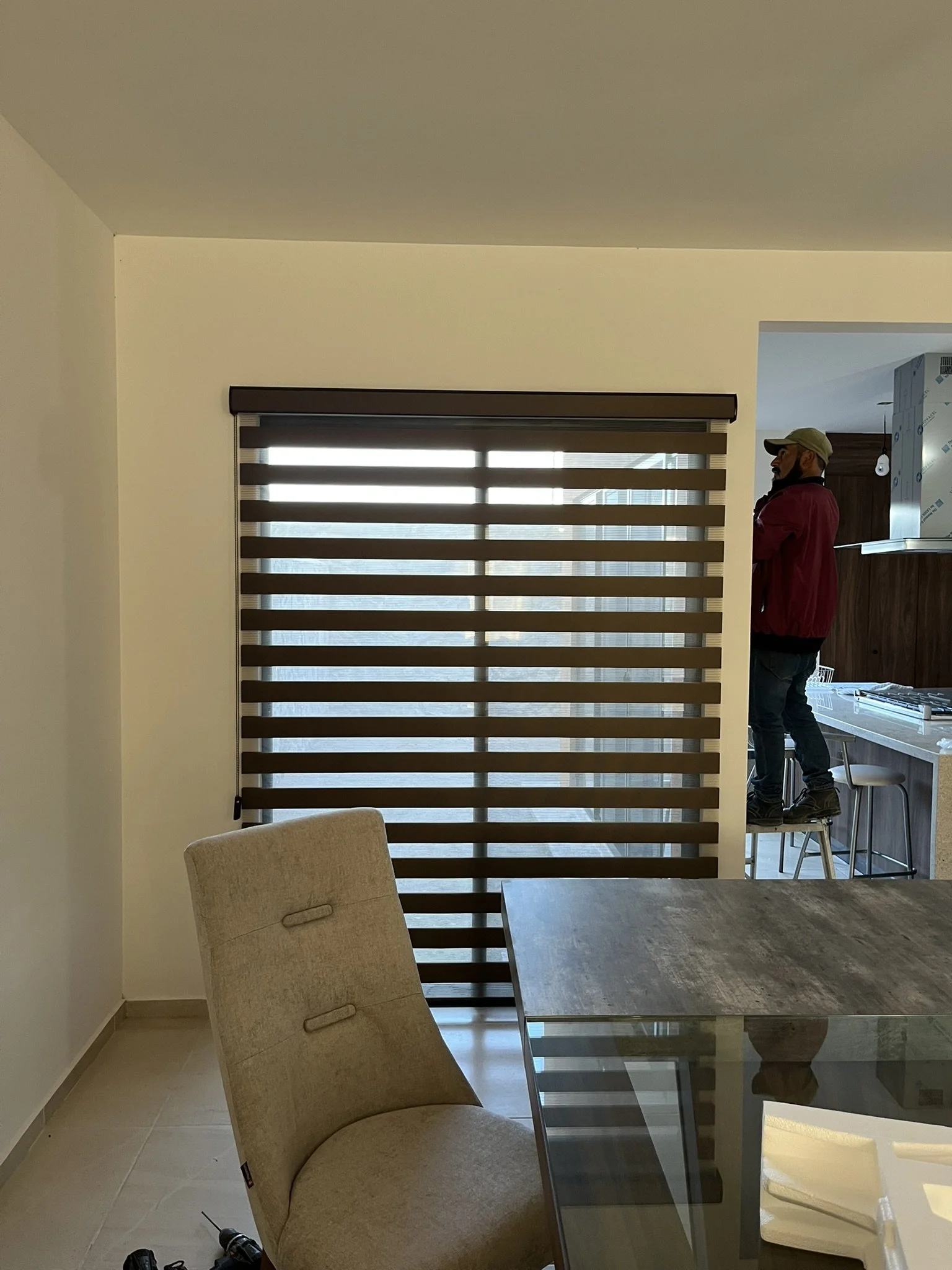 Interior de una sala con sillón beige, mesa de vidrio y ventana con persiana Sheer Elegance en tono chocolate. Departamento en San Miguel de Allende.
