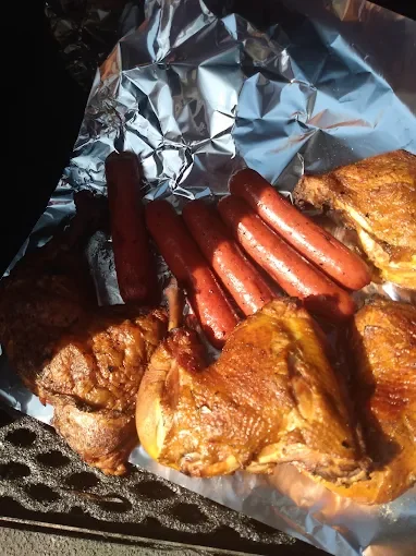 Cookout food with grilled chicken, hot dogs, and fried chicken pieces on aluminum foil.
