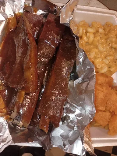 A meal with beef ribs, macaroni and cheese, and fried chicken pieces on a foil-lined tray.
