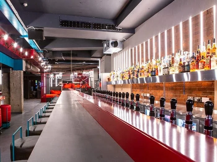 Tapped, Grafton Street, Dublin — Empty bar with a long counter, barstools, and shelves stocked with various bottles of alcohol in a modern, stylish setting.