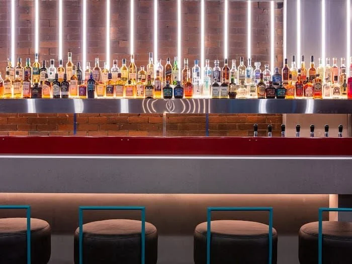 Tapped, Grafton Street, Dublin — Bar with an array of liquor bottles on a backlit shelf, bar stools in front, and a red bar counter in a modern, stylish setting.