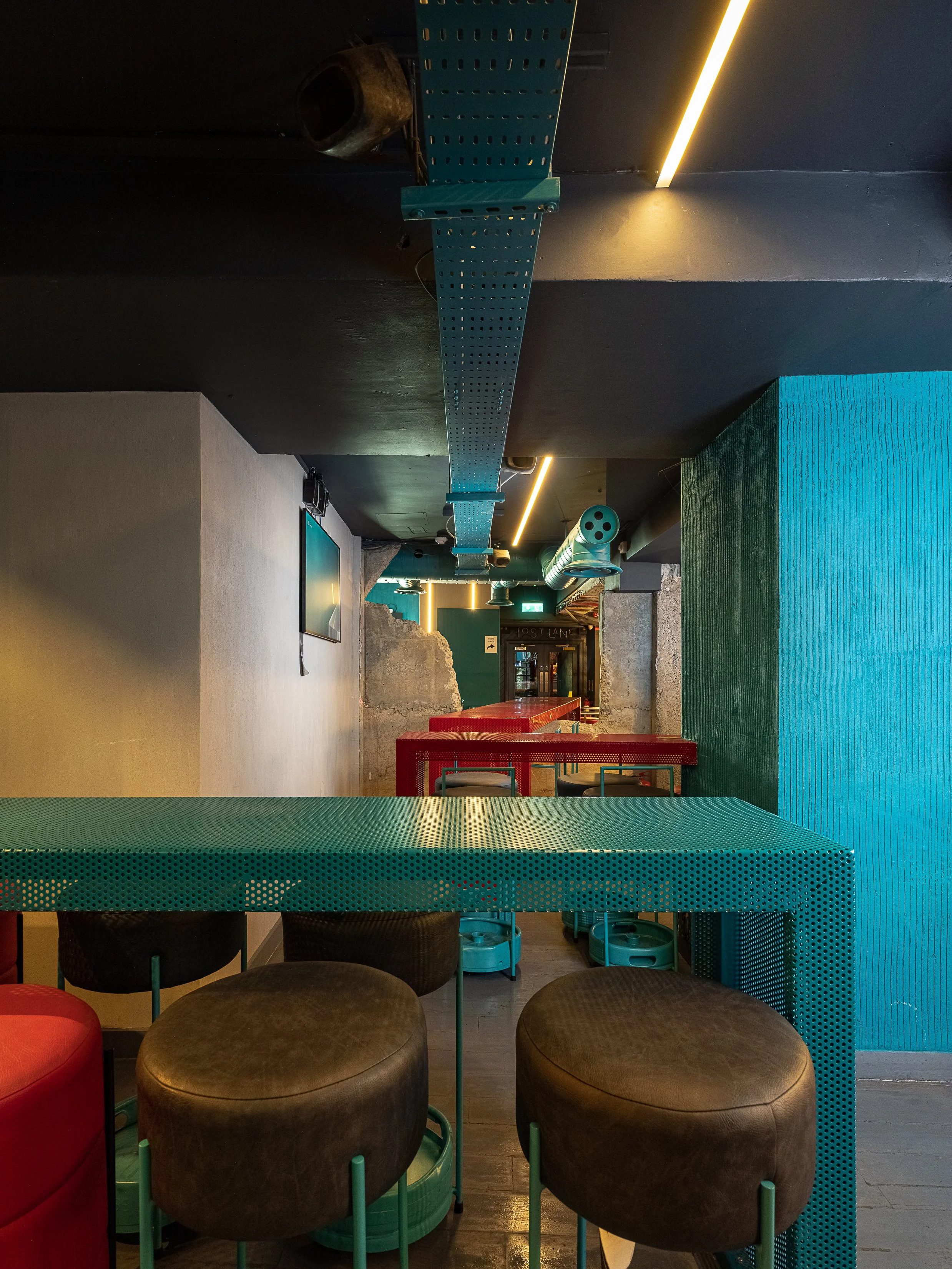 Tapped, Grafton Street, Dublin — Modern interior of a restaurant or cafe with black walls, unique teal-colored furniture, and circular stools in the foreground. There are exposed pipes and industrial-style lighting.