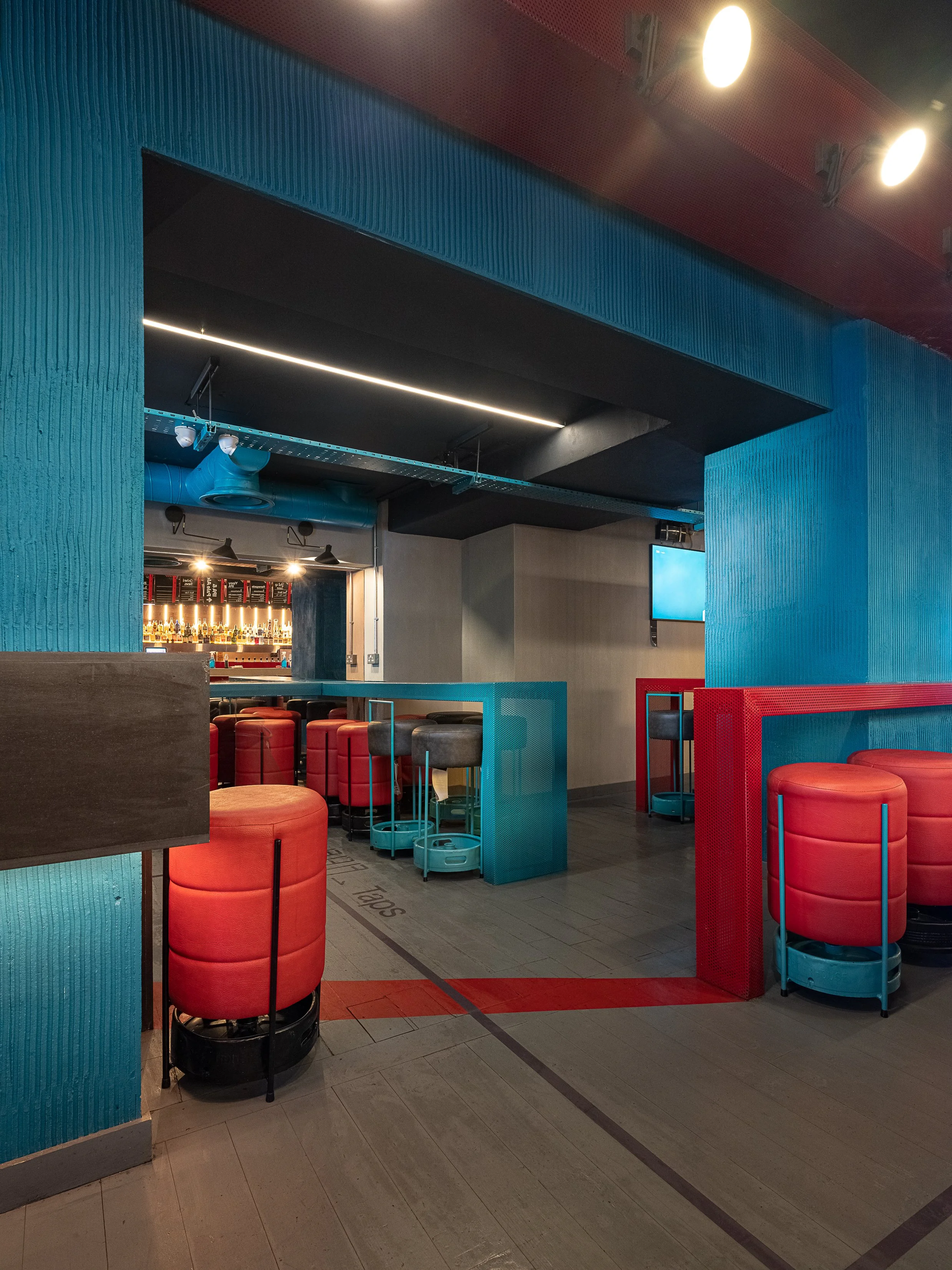 Tapped, Grafton Street, Dublin — Interior of a modern bar or restaurant with brightly colored blue and red furnishings, including red round stools and blue tables, with a bar area visible in the background featuring shelves with bottles.