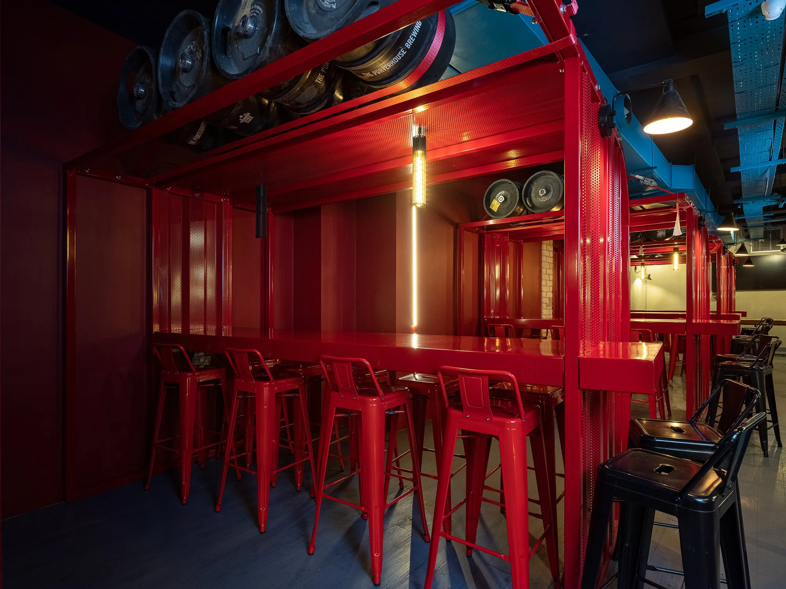Tapped, Grafton Street, Dublin — Red bar counter with high red chairs and black chairs around it in a dimly lit restaurant or bar with exposed brick wall and hanging lights.