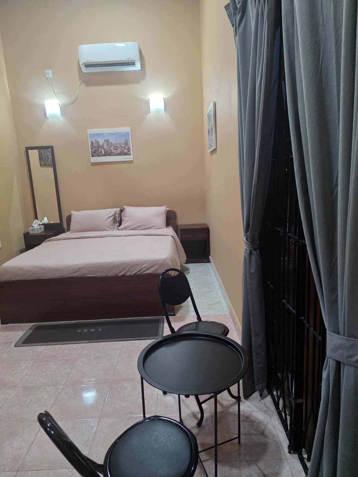 Hotel room with a bed, nightstand, mirror, wall art, curtains, and small round tables with chairs.