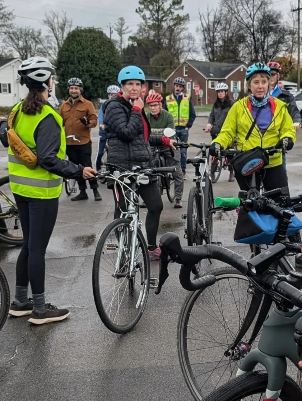 Ellen with a group of people gathered outdoors with their bicycles, wearing helmets and cycling gear, preparing for a ride.