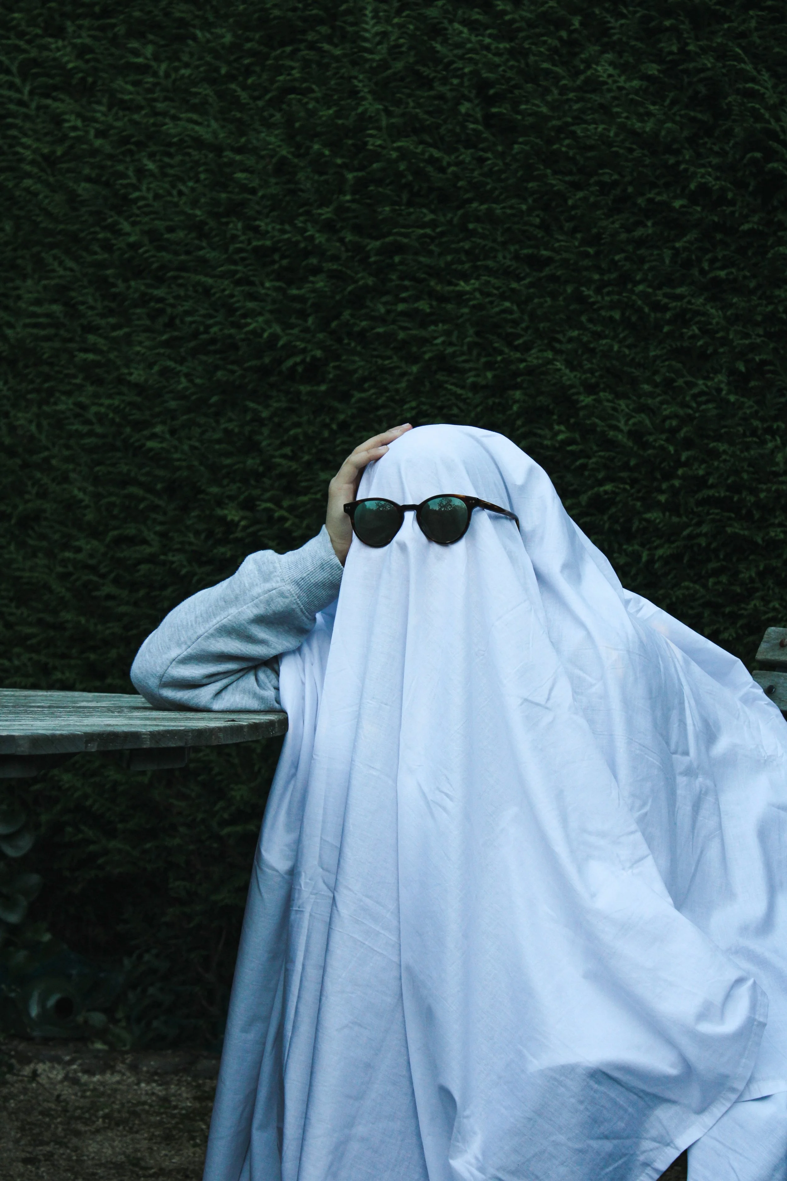 A person in a simple ghost costume and sunglasses looks chagrined.