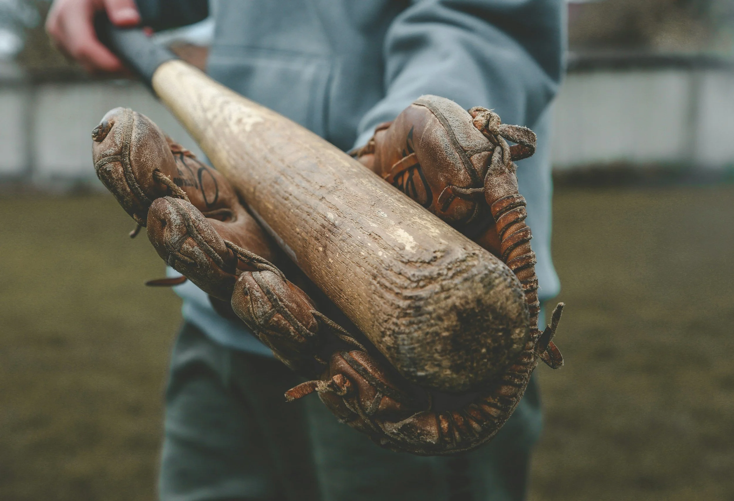 Person wearing gloves holding an old baseball bat wrapped with barbed wire.