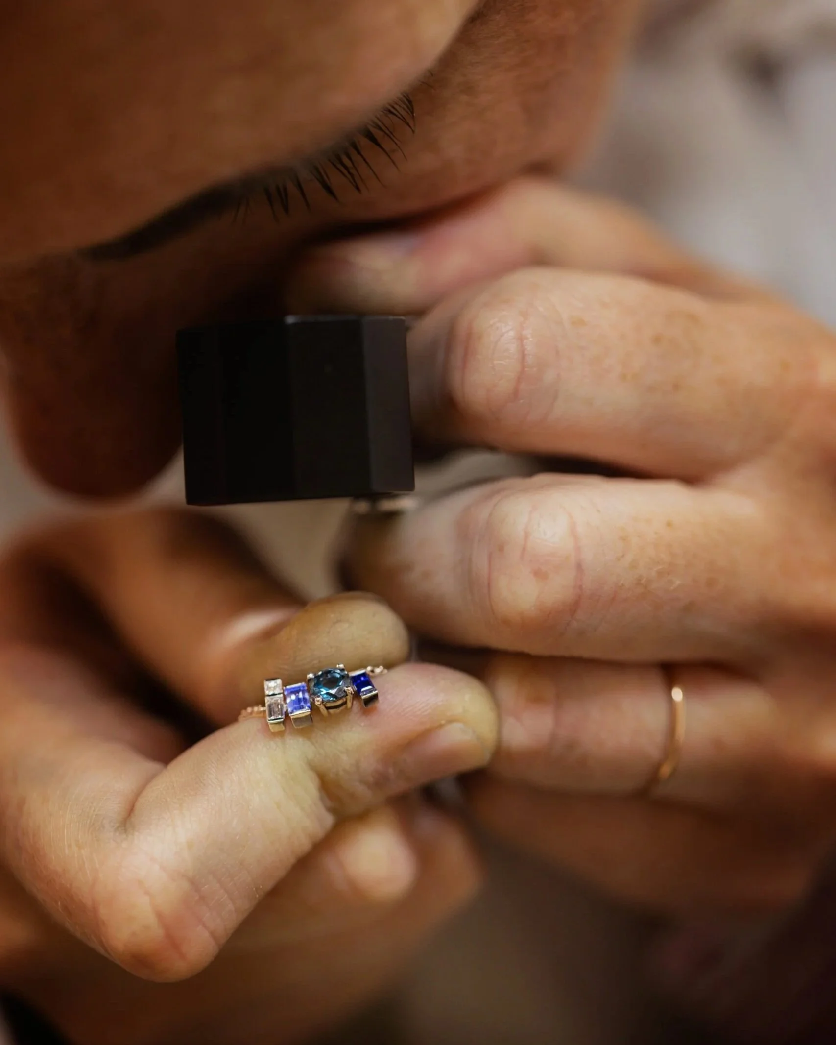 Une personne portant une bague avec des pierres précieuses bleues et une autre personne avec un bracelet doré, le tout vu de près.