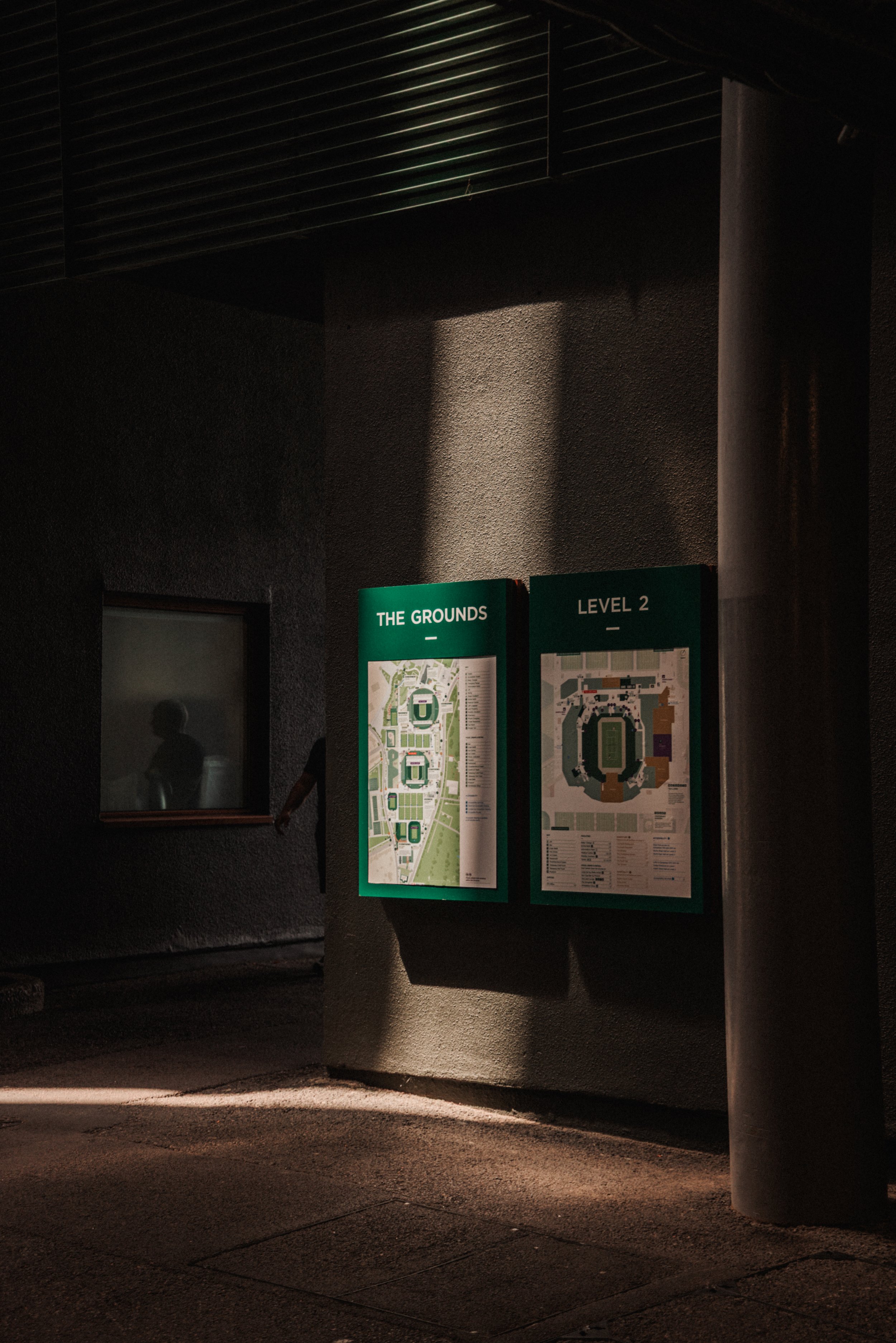 Deux panneaux d'information verticaux sur un mur extérieur, affichant des plans du stade et de la zone environnante, sous un éclairage nocturne.