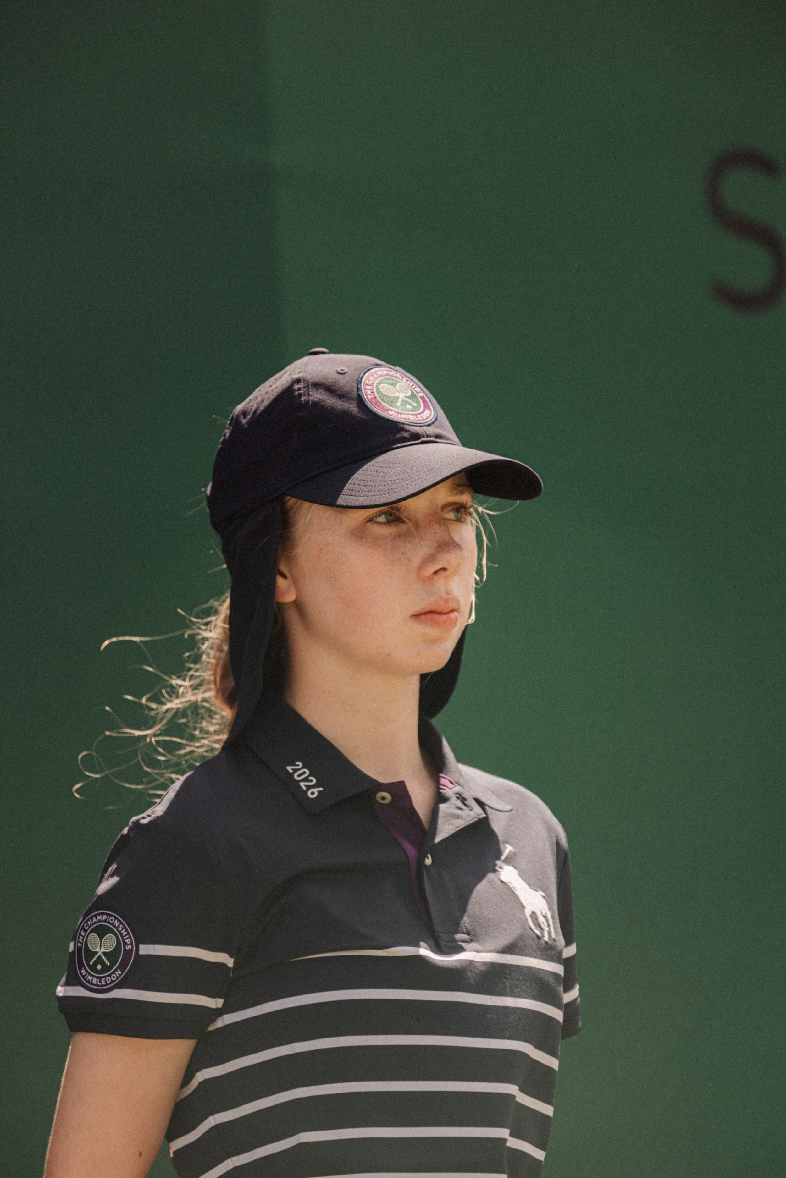 Jeune femme professionnel de tennis portant un chapeau de Wimbledon, vêtue d'une chemise à rayures avec le logo de Wimbledon sur la manche, lors d'une compétition.