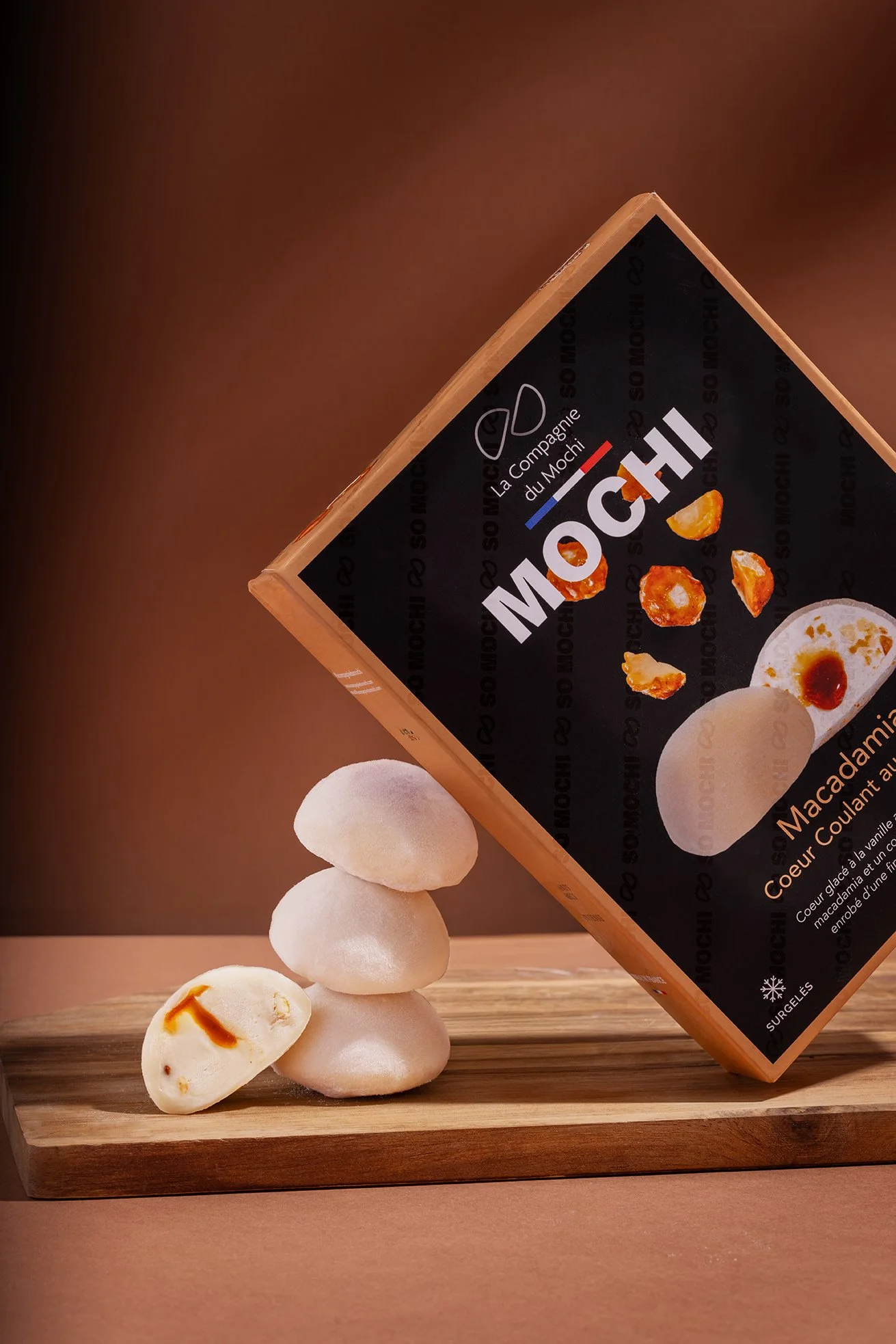 Boîte de macarons au cœur glacé à la vanille et caramel, avec quelques macarons empilés sur une planche en bois.