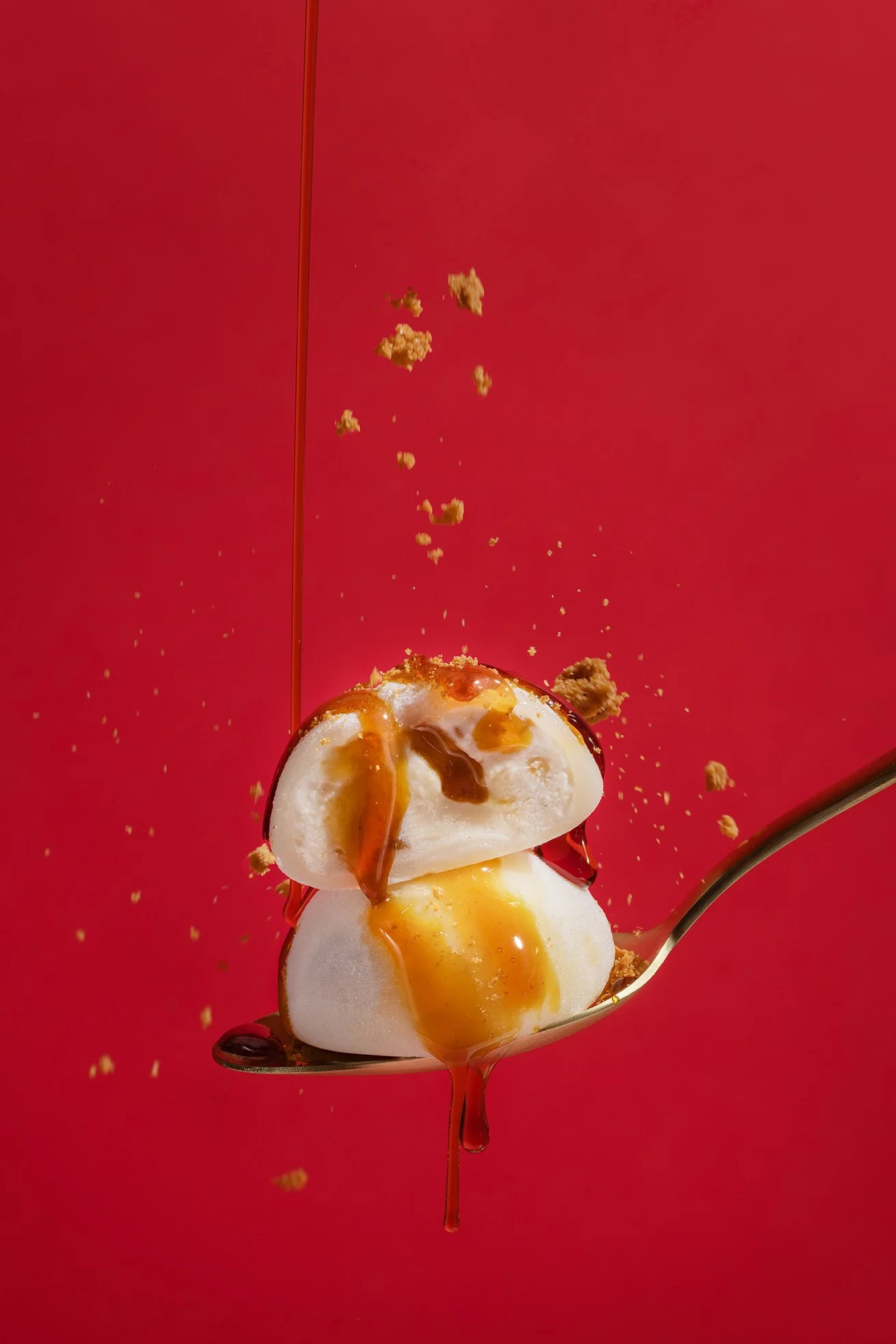 Une cuillère contenant des œufs pochés, de la sauce, des morceaux de bacon ou de jambon, et de la chapelure, avec une sauce versée au-dessus, contre un fond rouge.