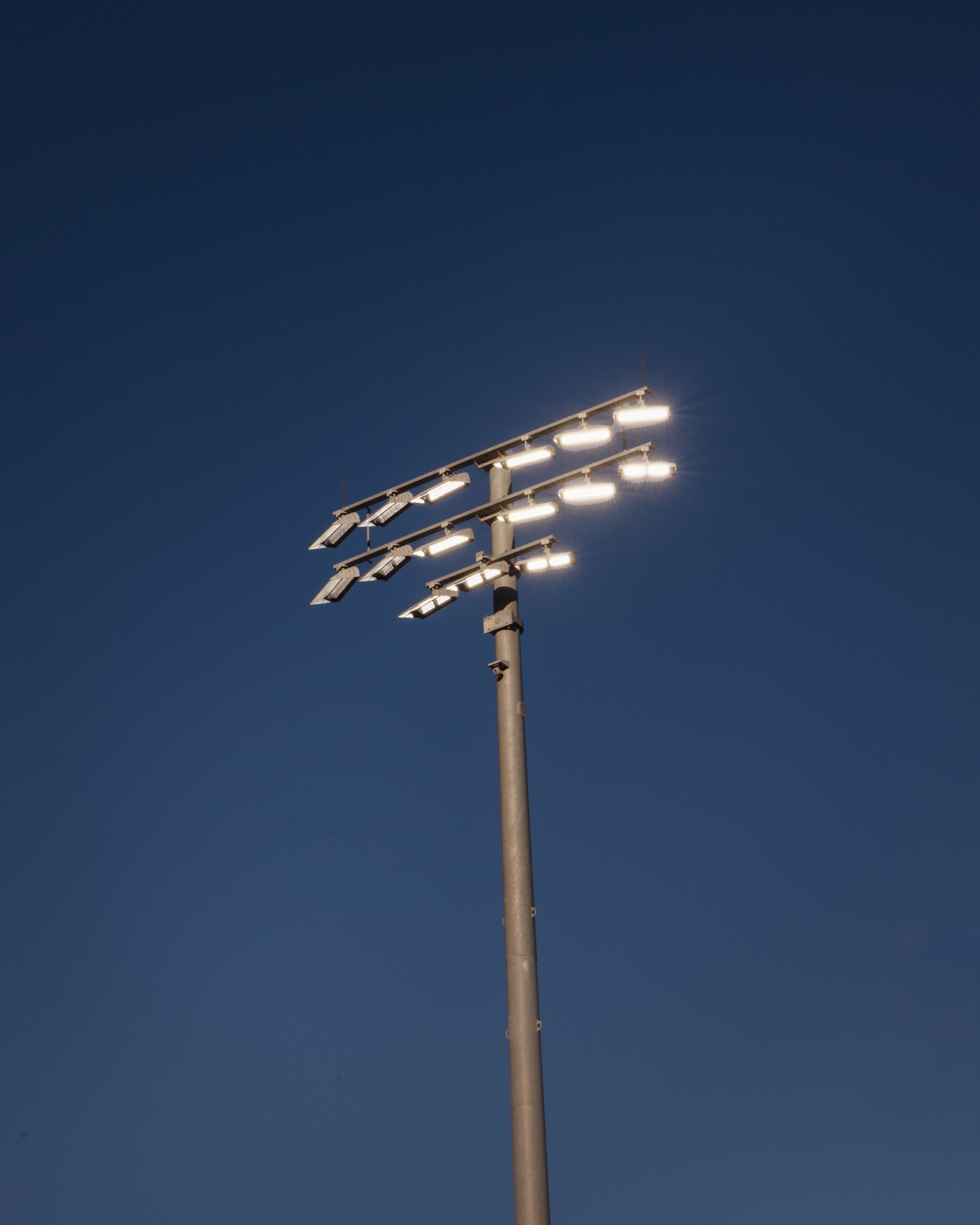 Panneau d'éclairage public avec plusieurs lampes allumées sous un ciel sombre.