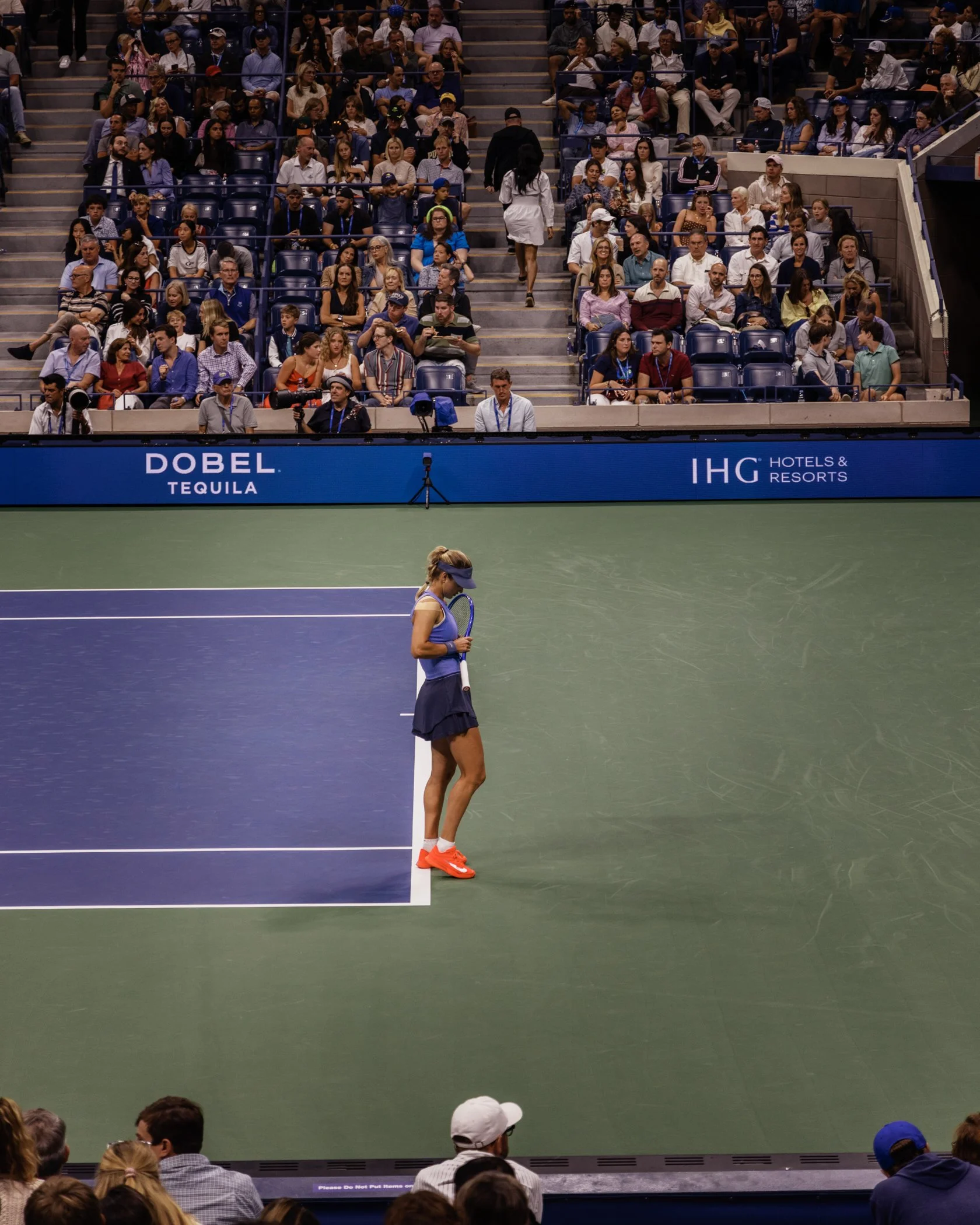 Une joueuse de tennis se tient seule sur le court, face à un public attentif assis dans les gradins.