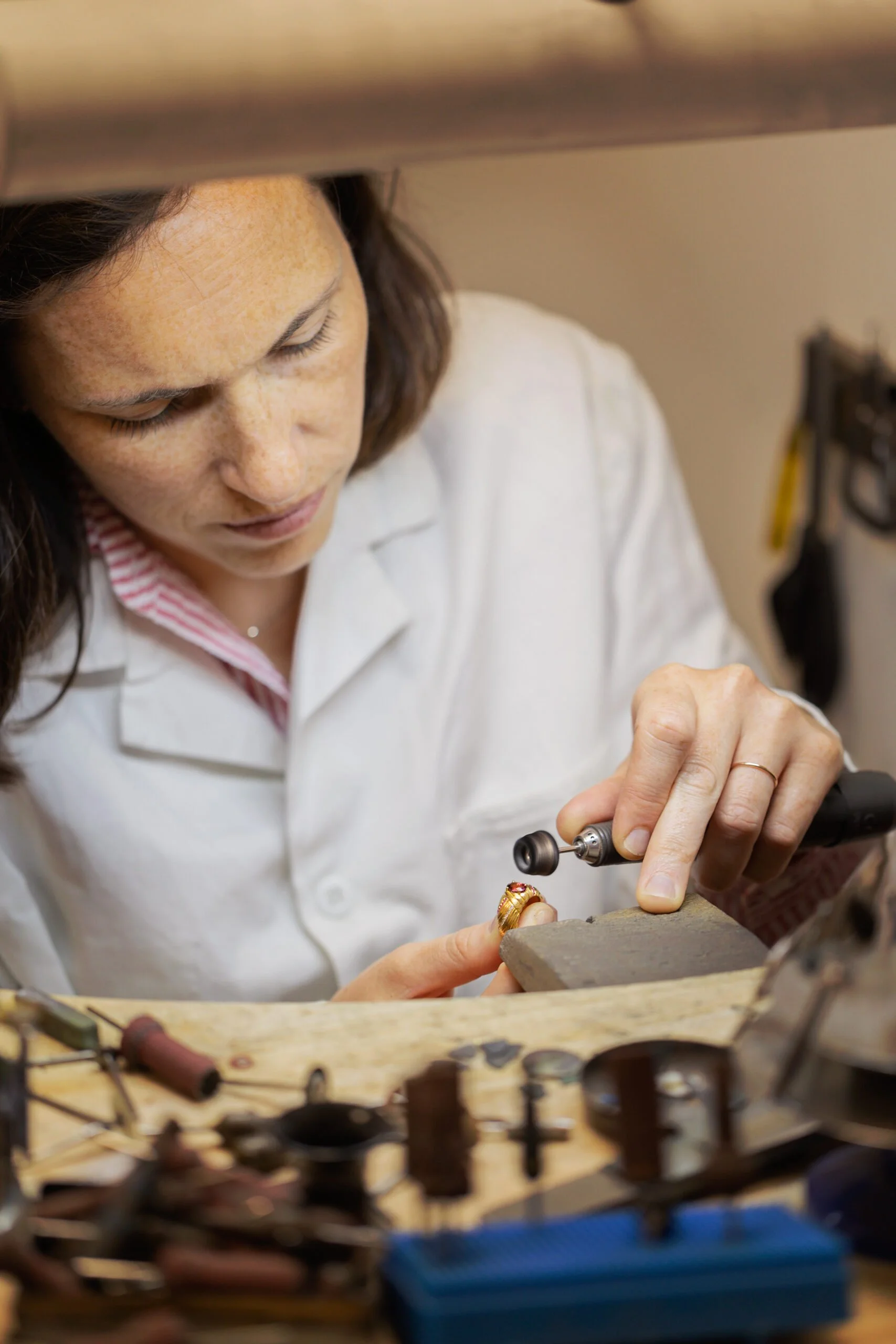 Une femme travaille sur la restauration de bijoux anciens en utilisant des outils de joaillerie.