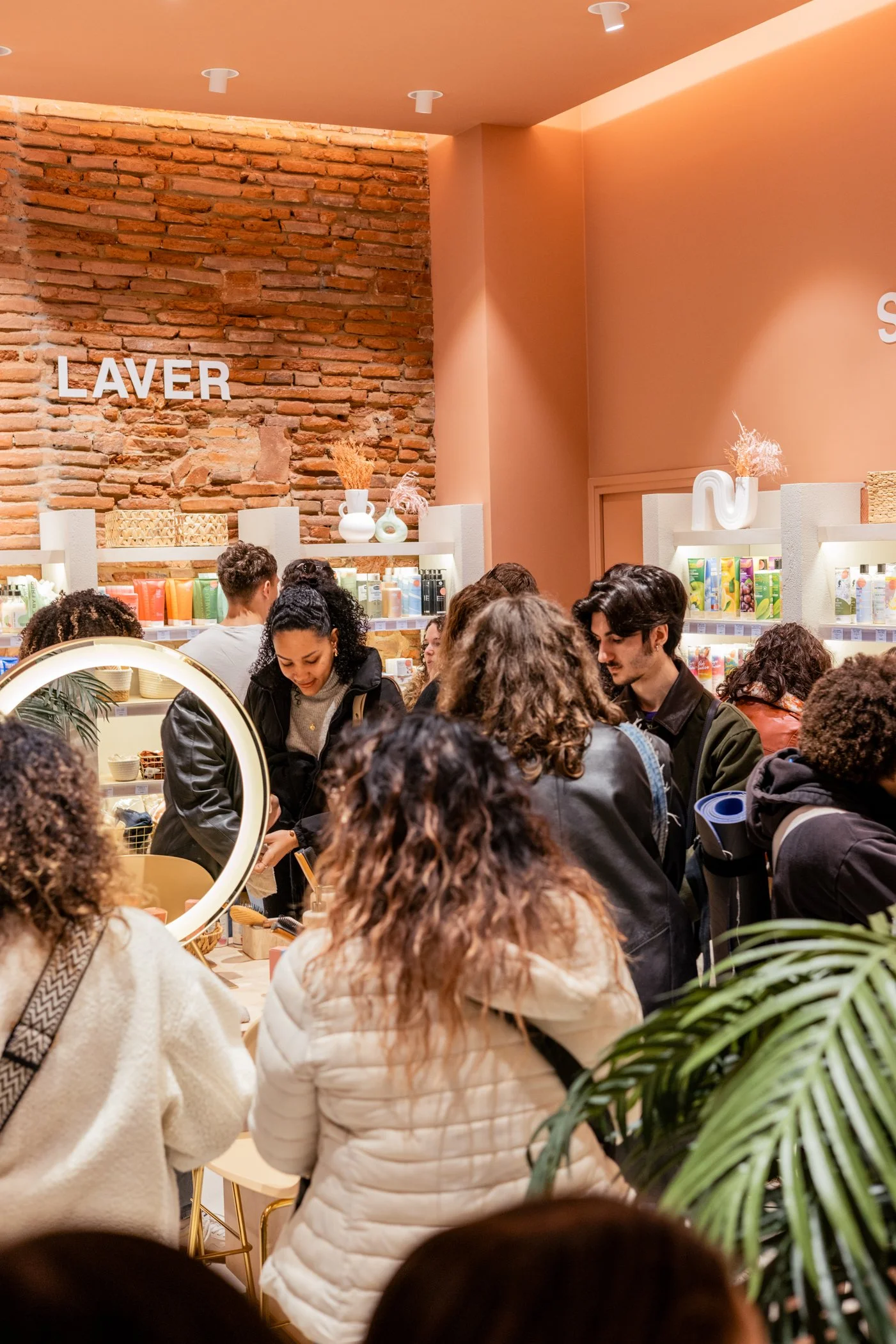 Une foule de personnes dans un magasin, beaucoup de sacs et une ambiance animée, avec un mur en briques apparentes et des étagères avec des produits.