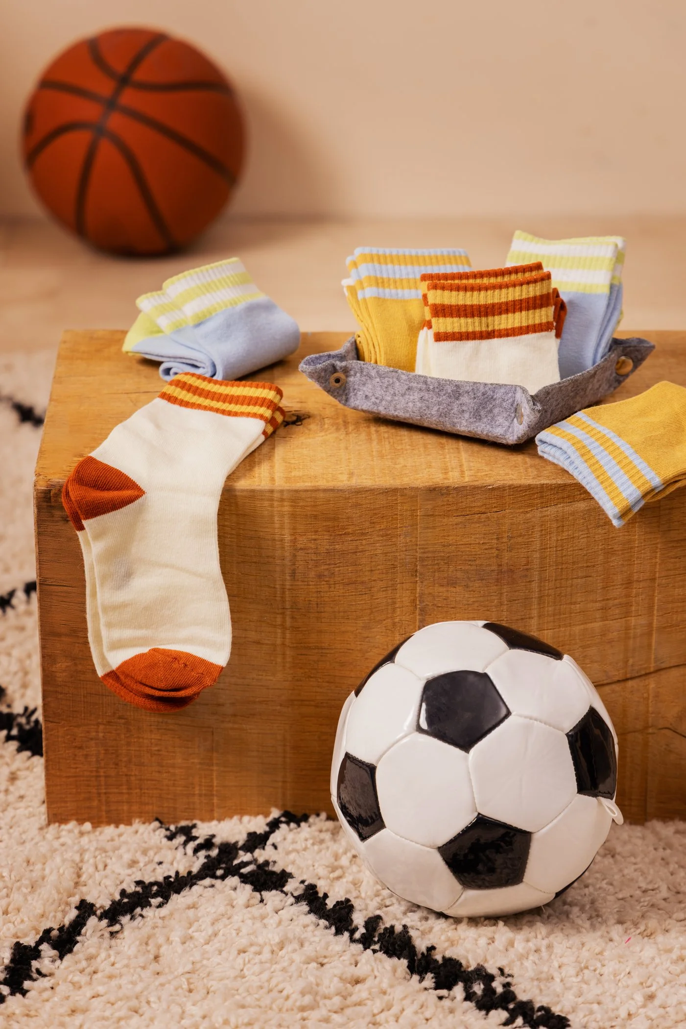 Ballon de basketball, chaussettes colorées, ballon de football, et tapis moelleux avec motifs noirs.