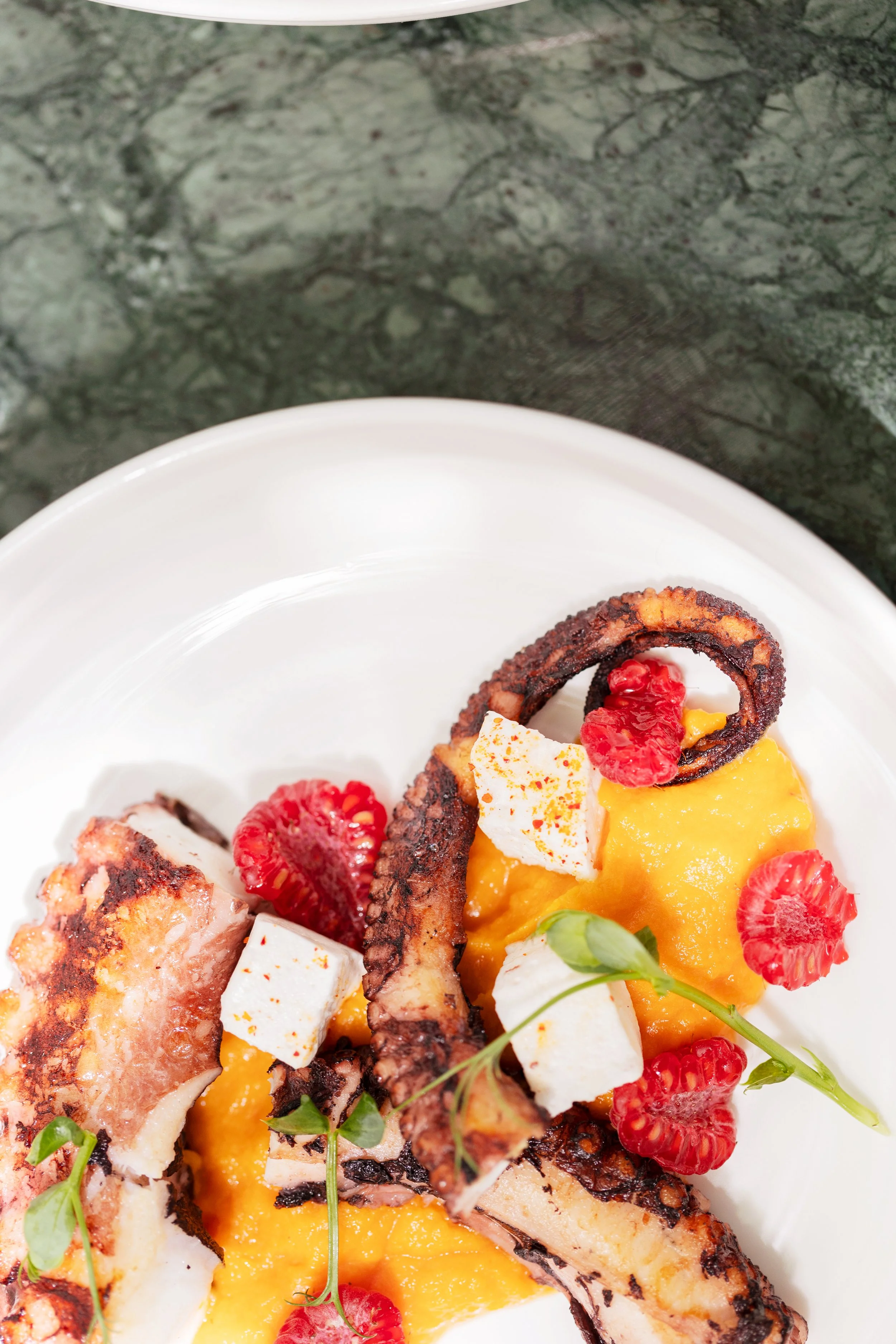 Assiette avec du poisson grillé, de la purée de mangue, et des fruits rouges, décorée de microgreens.