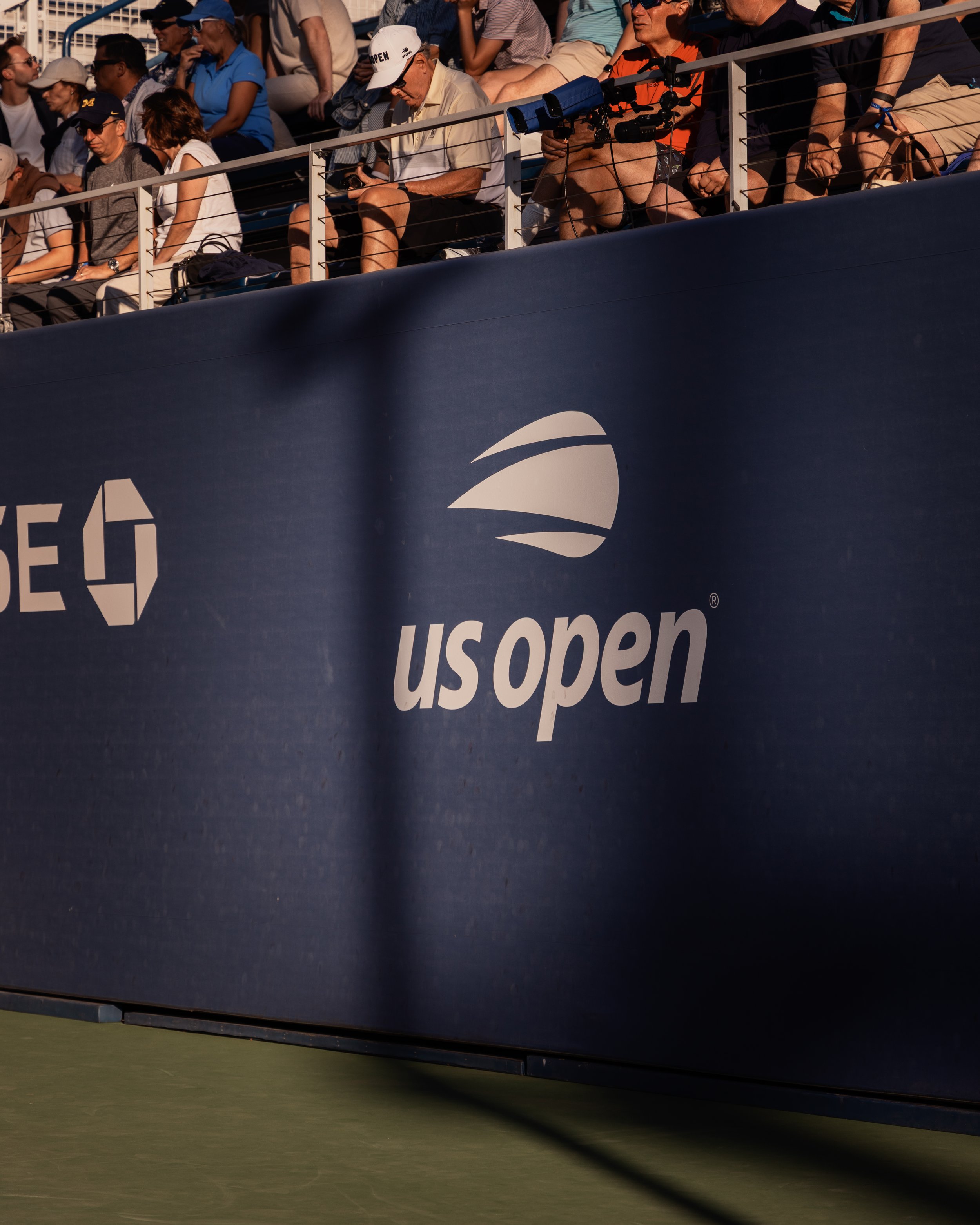 Spectateurs assis dans les gradins lors d'un événement à l'Open de tennis, portant des vêtements décontractés près du terrain.
