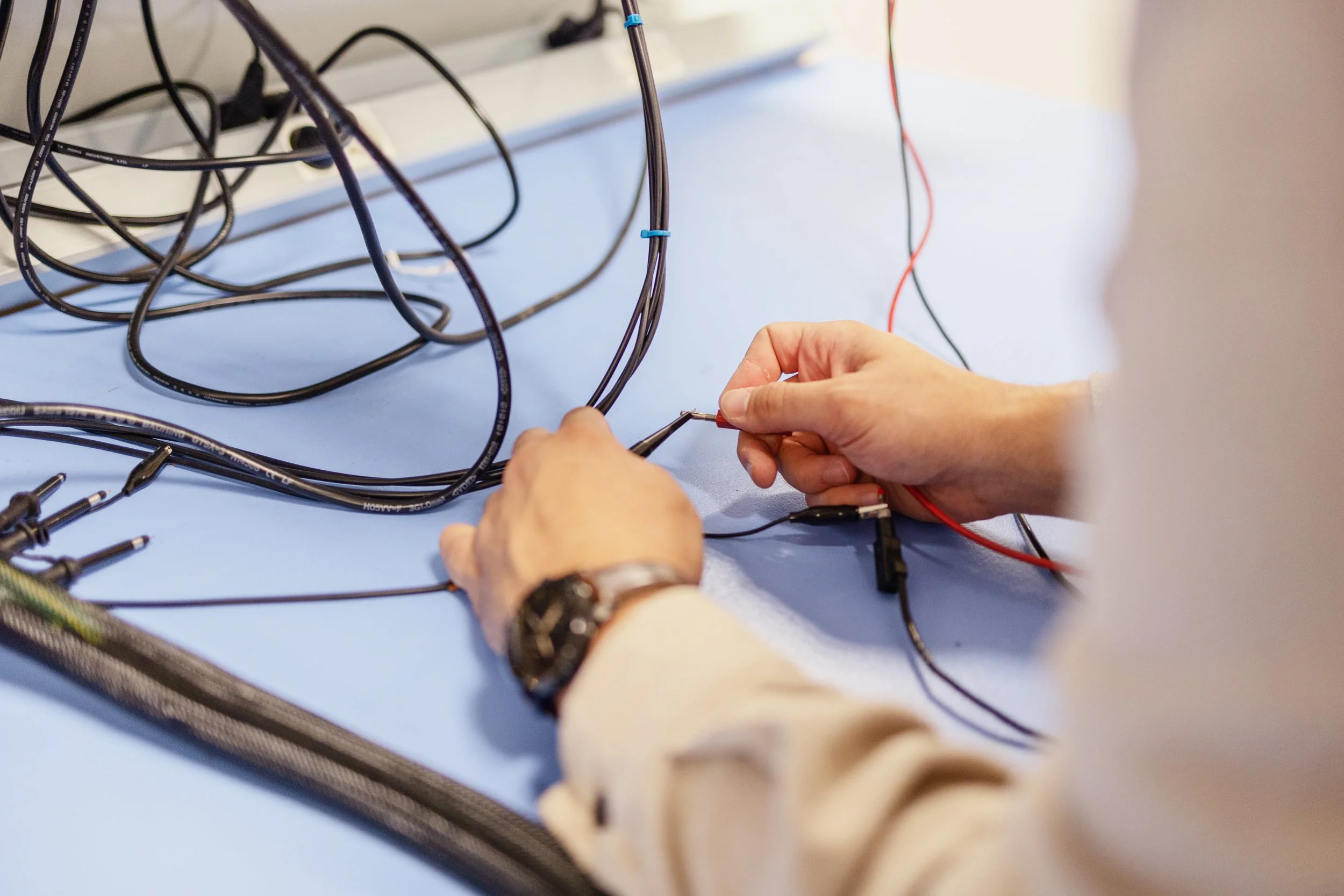 Une personne manipule des fils électriques sur une table bleue, dans un environnement technique ou de laboratoire.