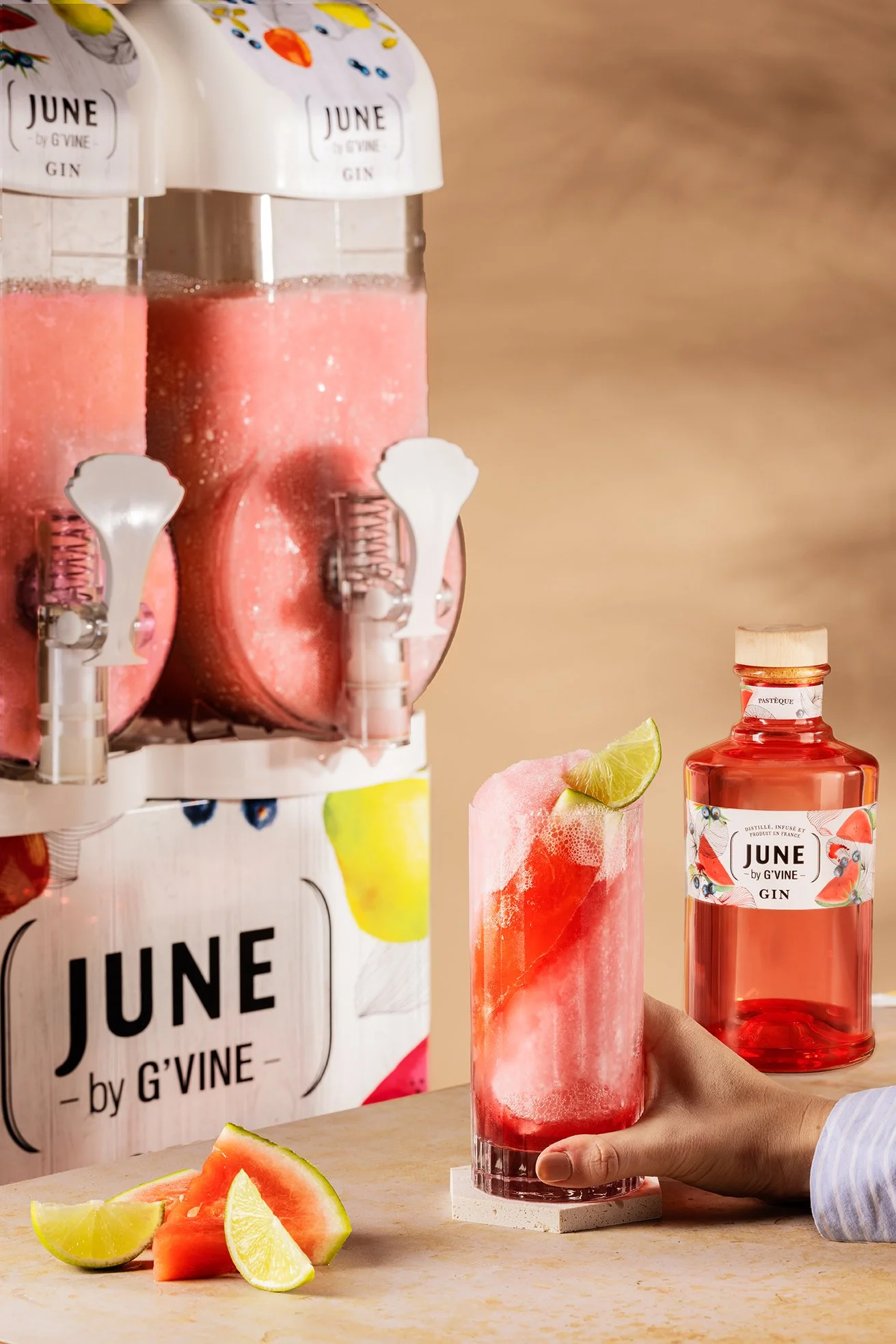 Un verre de cocktail rose à la pastèque avec une tranche de citron vert sur le bord, dans la main d'une personne.