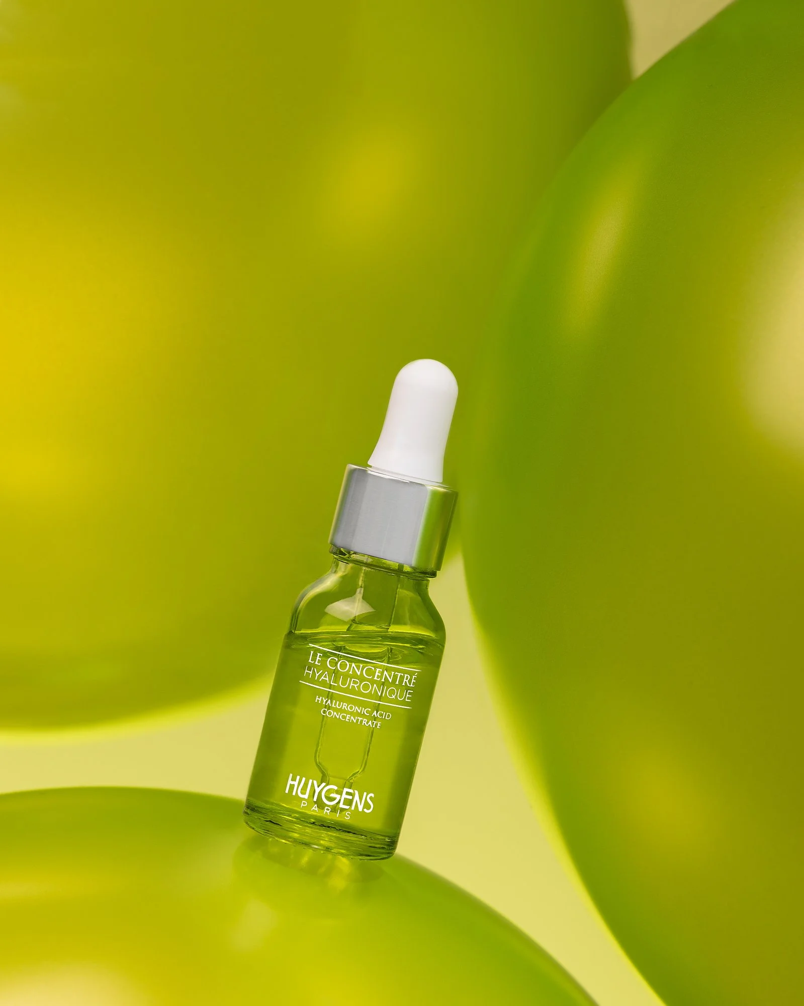 Une bouteille de concentré d'acide hyaluronique avec un bouchon blanc, placée contre un fond vert