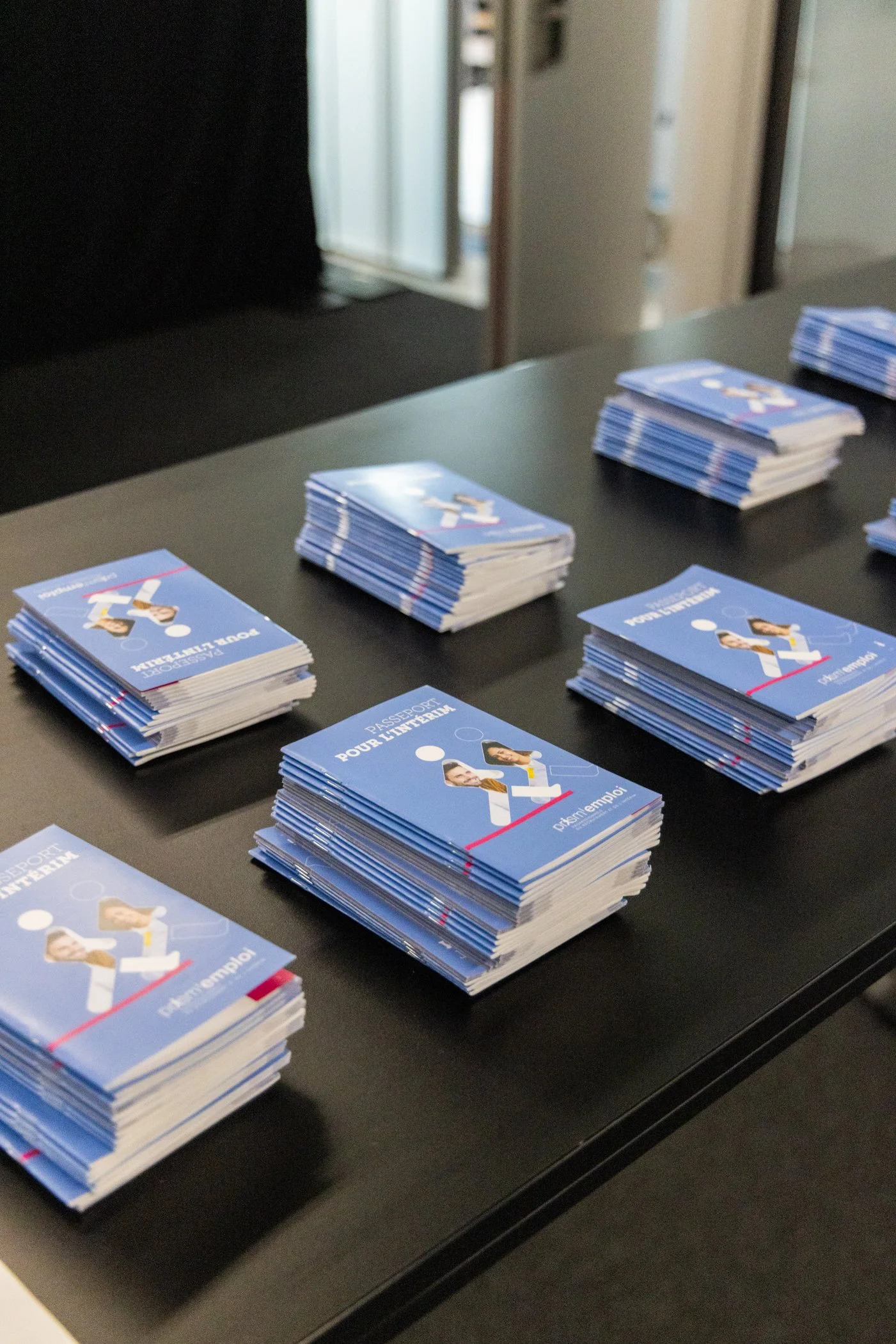 Plusieurs piles de brochures bleues avec des illustrations de personnes debout, disposées sur une table noire.