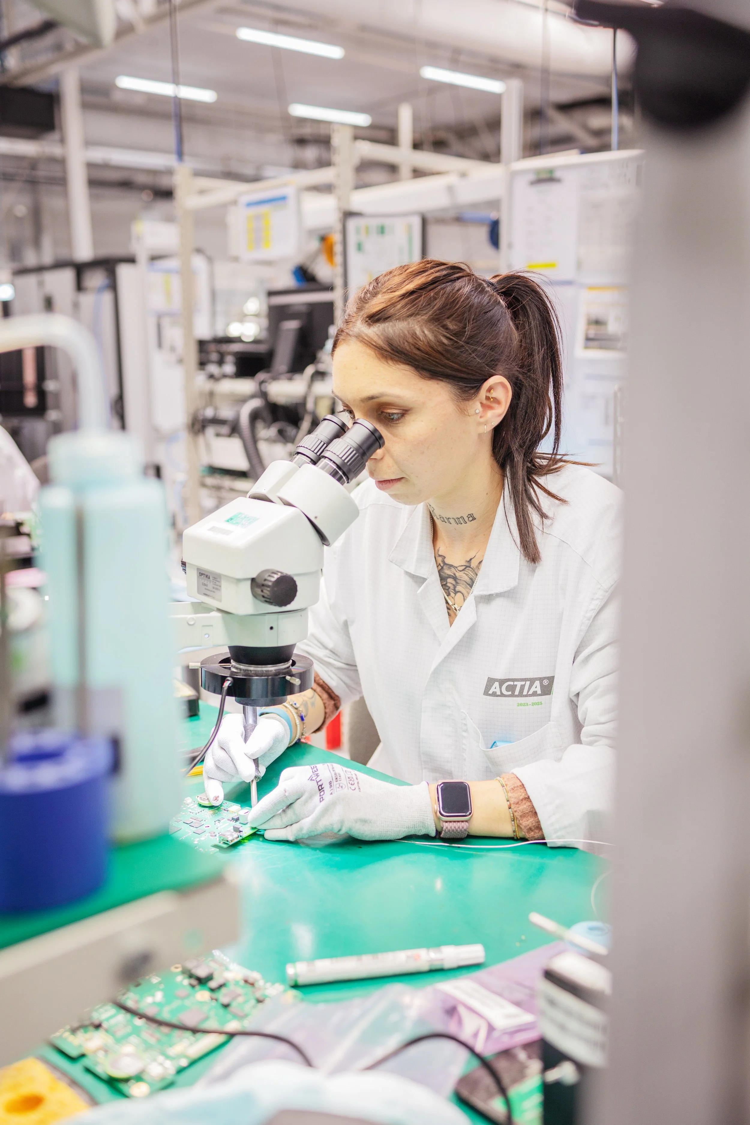 Une femme utilisant un microscope dans un laboratoire, travaillant sur un circuit imprimé.