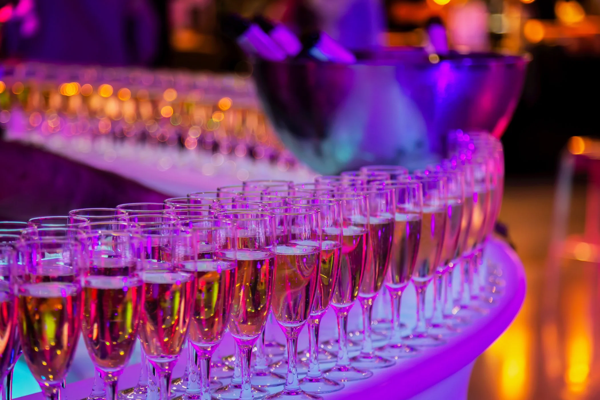 Verres à champagne avec une lumière colorée violette et rose. En arrière-plan, un seau à glaçons et d'autres éléments de décoration pour une fête ou un événement.
