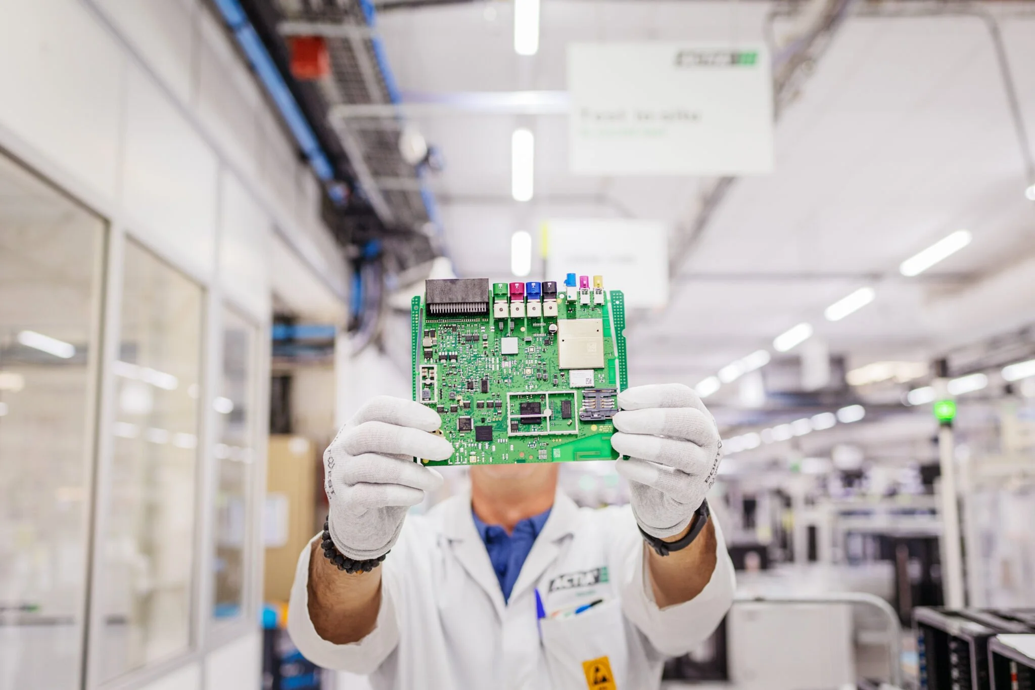 Technicien en laboratoire tenant une carte électronique en salle blanche.