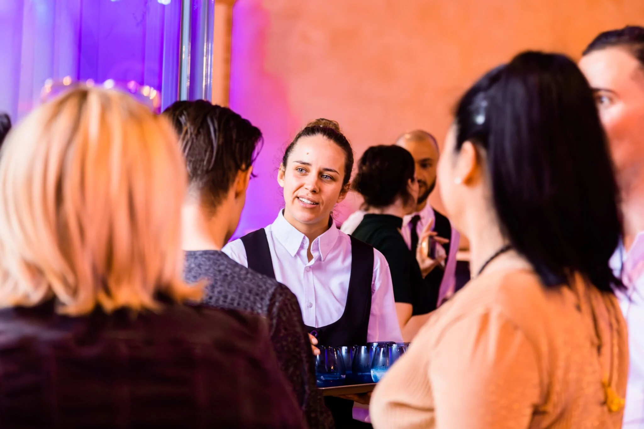 Groupe de personnes discutant lors d'une réception ou fête, ambiance colorée avec éclairage violet et orange.