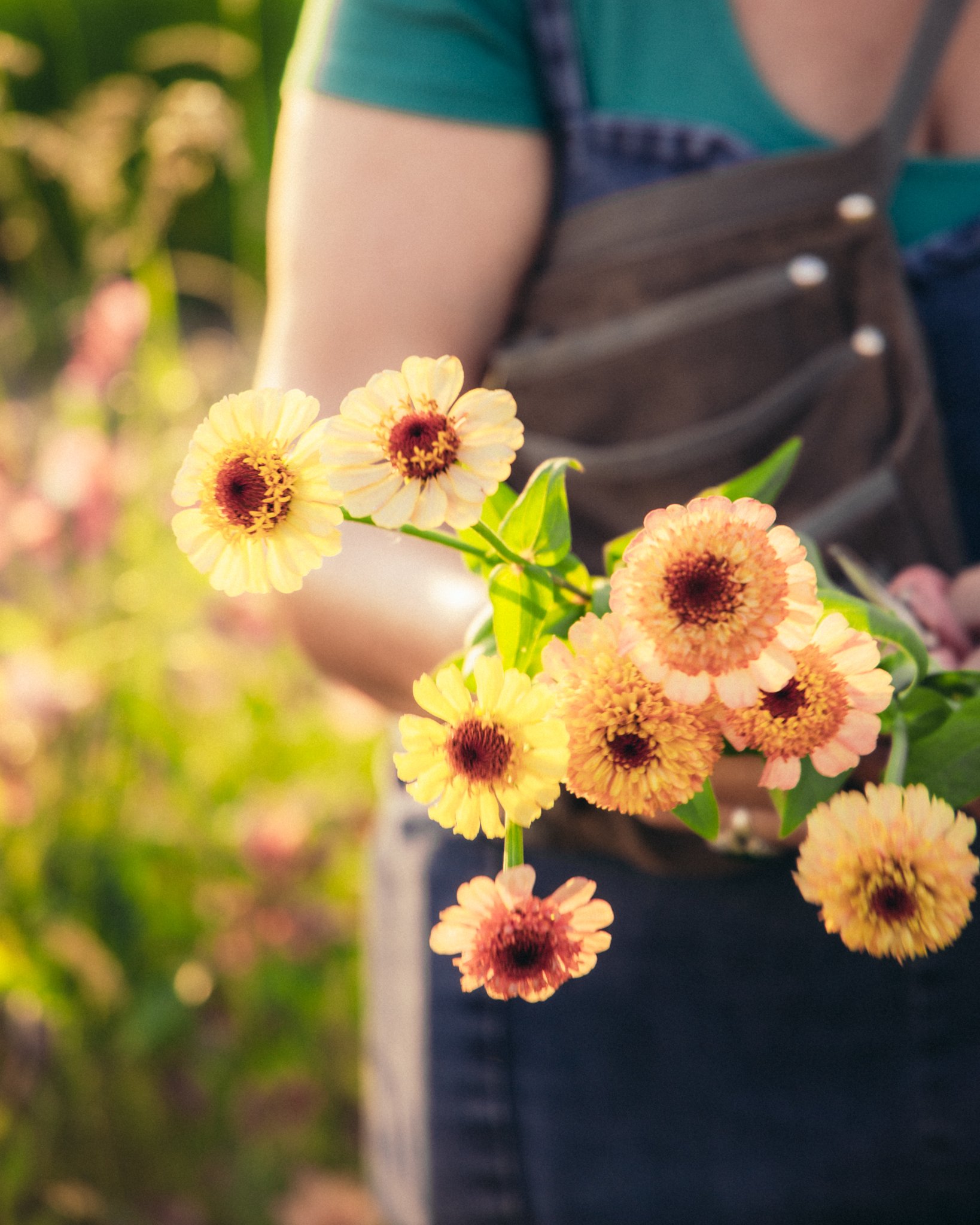 Fleurs jaunes et orange dans un bouquet, avec une personne en arrière-plan portant un vêtement vert et un sac à dos.