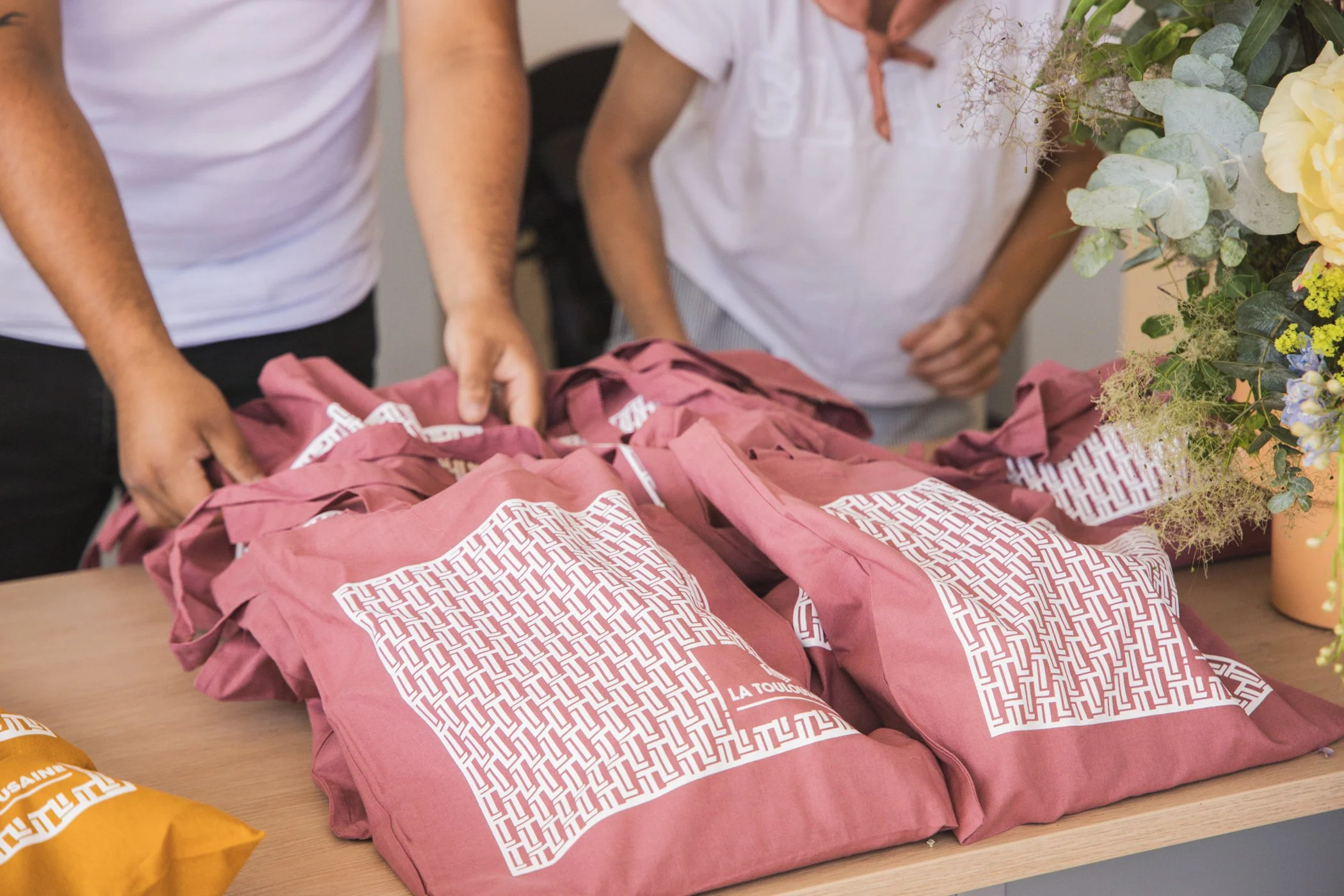 Paquets en papier rose disposés sur une table, entourés de fleurs et de petits sacs orange.