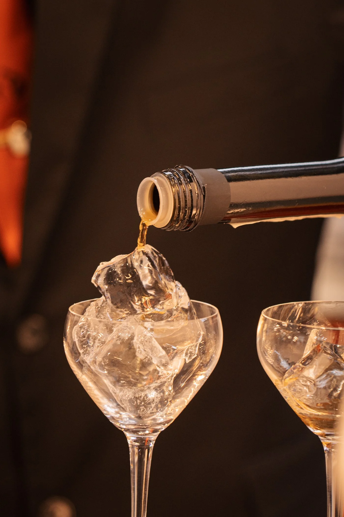 Une bouteille de champagne verse un liquide dans un verre à vin rempli de glaçons.