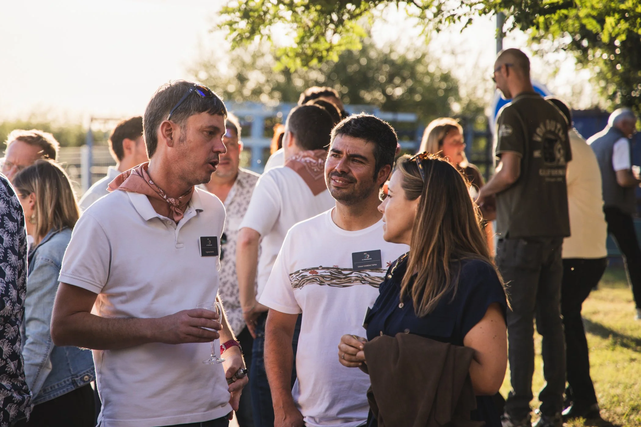Groupe de personnes conversant lors d'un événement en plein air en fin d'après-midi, avec des arbres en arrière-plan