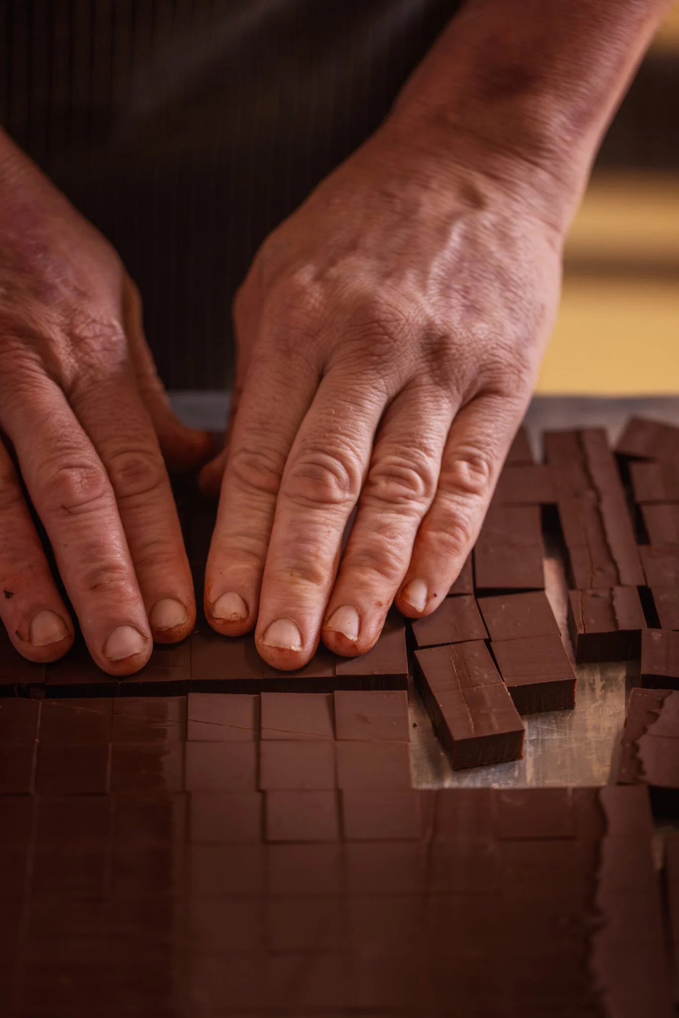 Mains d'une personne manipulant des carrés de chocolat sur une surface de travail.